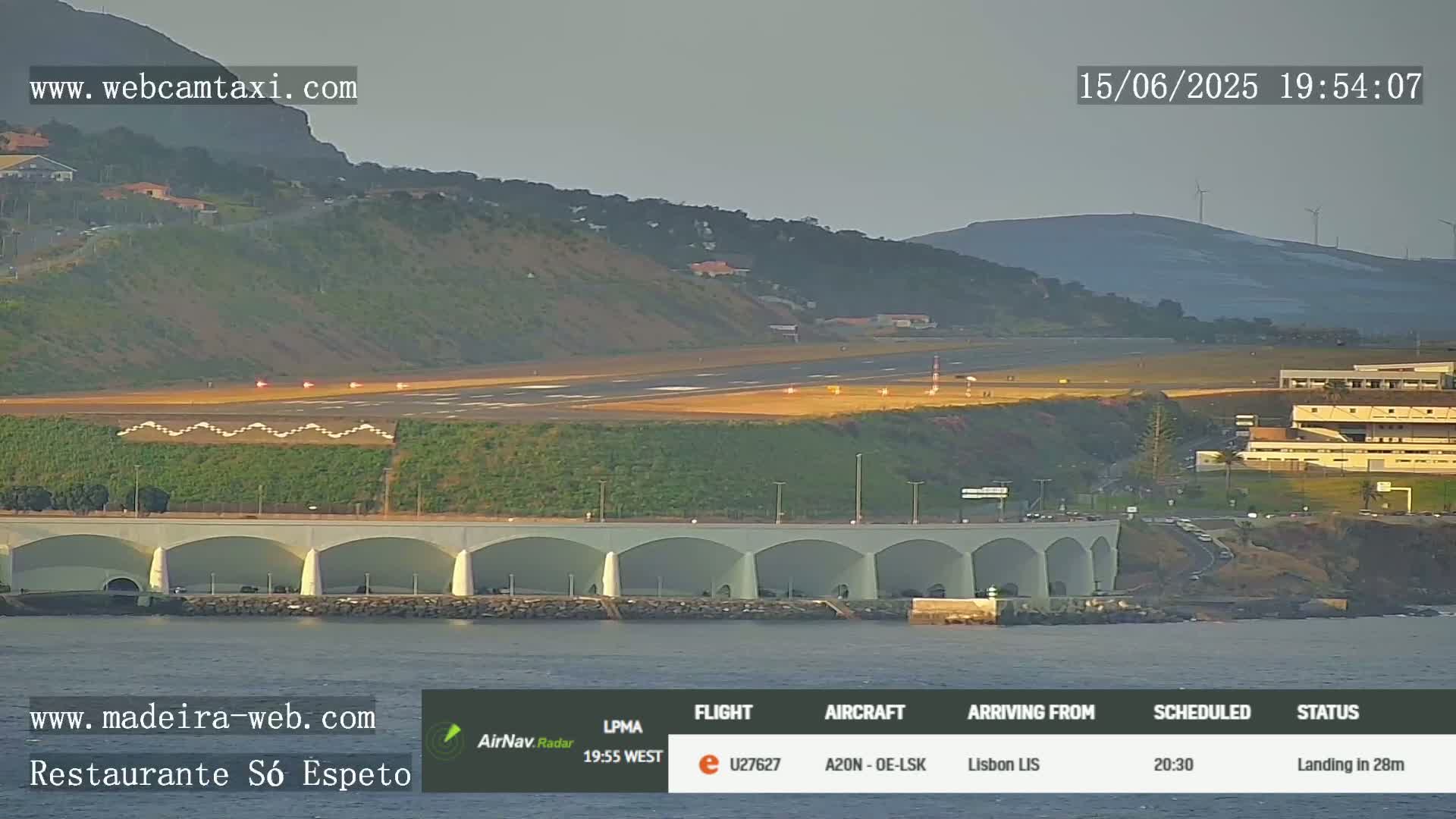 An airport runway and terminal are visible near a coastline under a clear sky, with a structure featuring arched alcoves along the water's edge.
