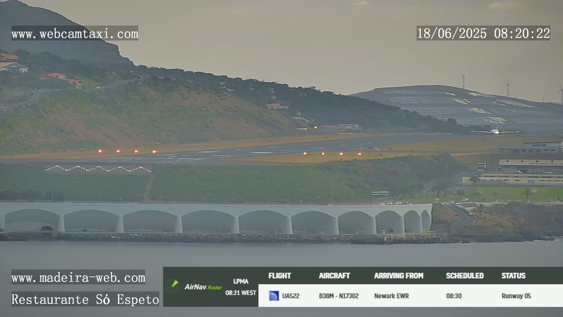 An airplane is landing on a runway near a body of water under an overcast sky.