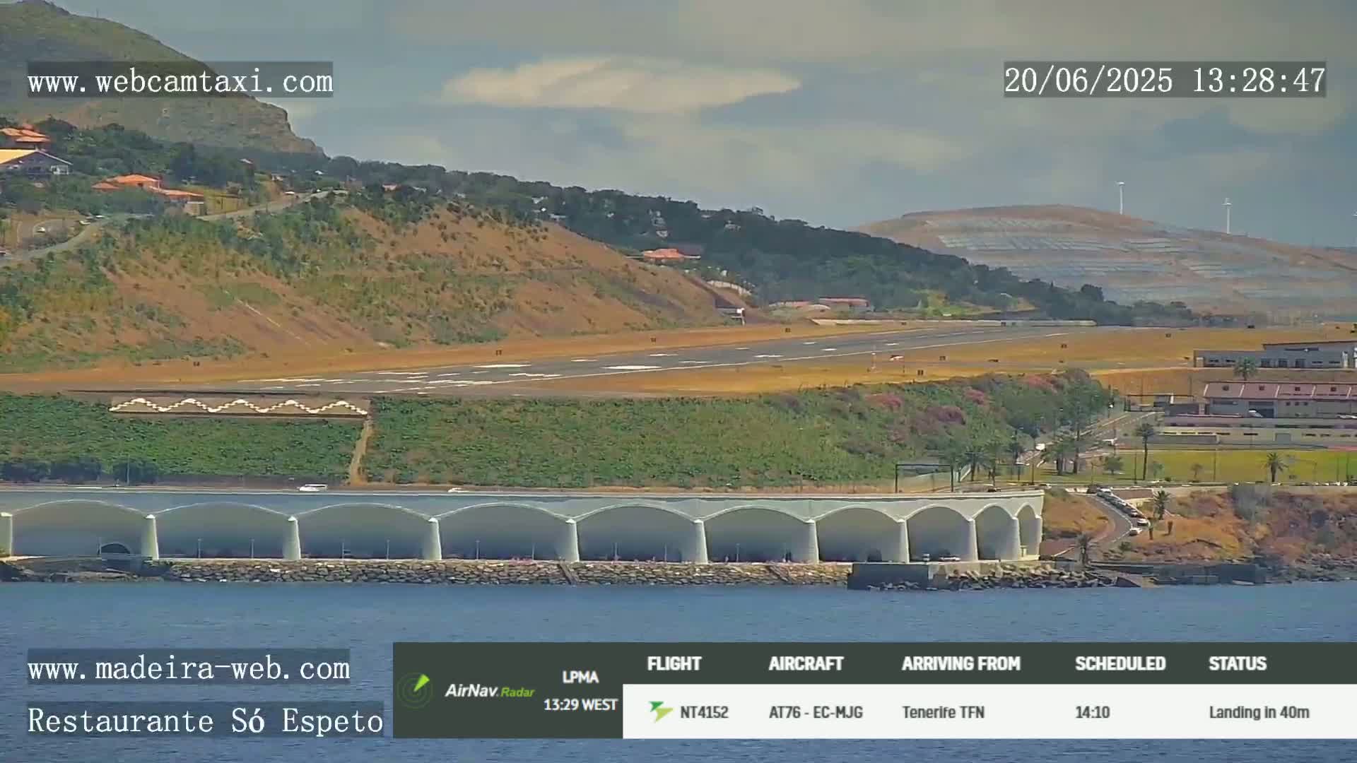 An airplane is landing at an airport next to the ocean under partly cloudy skies.