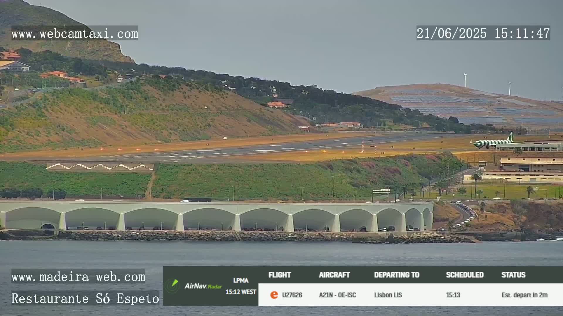 An airplane is taking off from an airport runway near a body of water, under overcast skies.