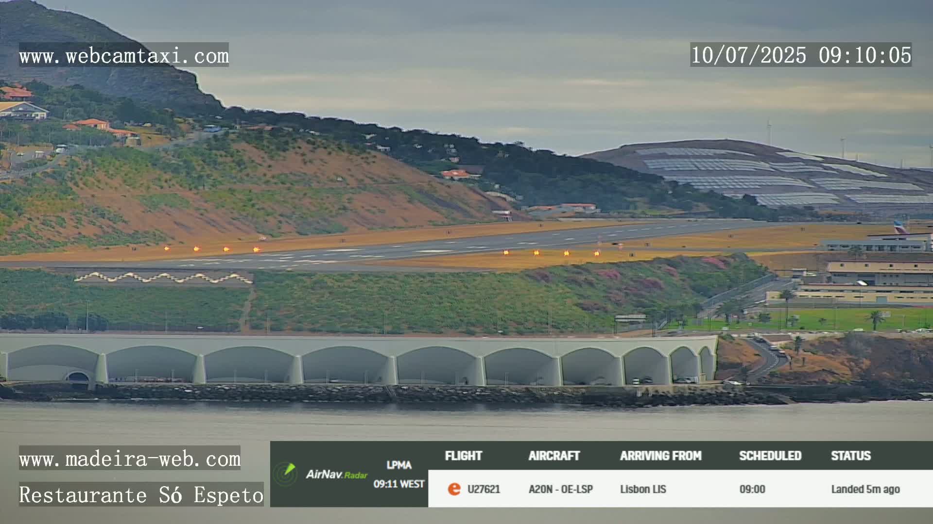 An airplane has just landed on a runway next to a calm body of water, with overcast skies and hills in the background.