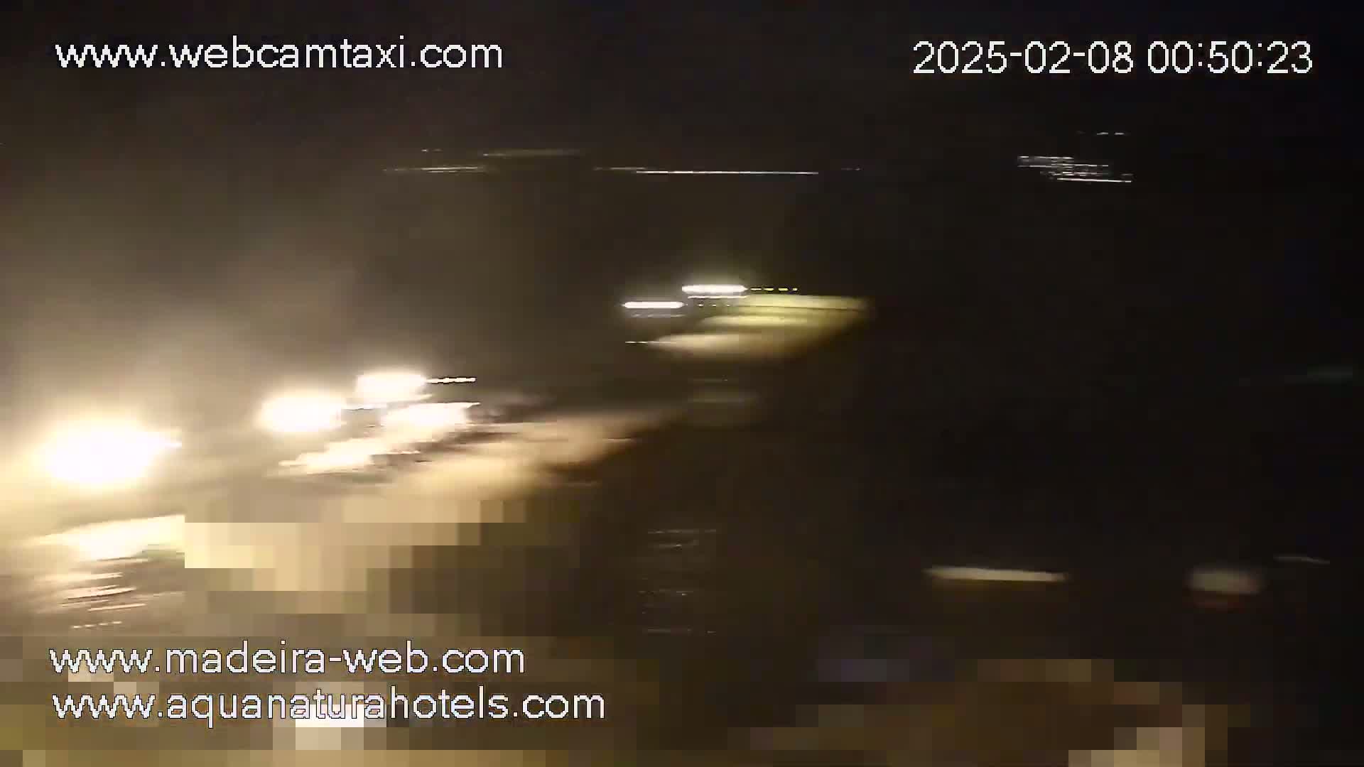 At night, blurry headlights from several vehicles are visible on a dark road.