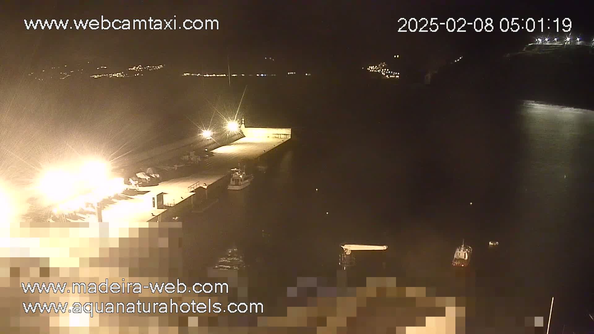 A brightly lit dock at night with several boats moored alongside, overlooking dark water under a clear sky.