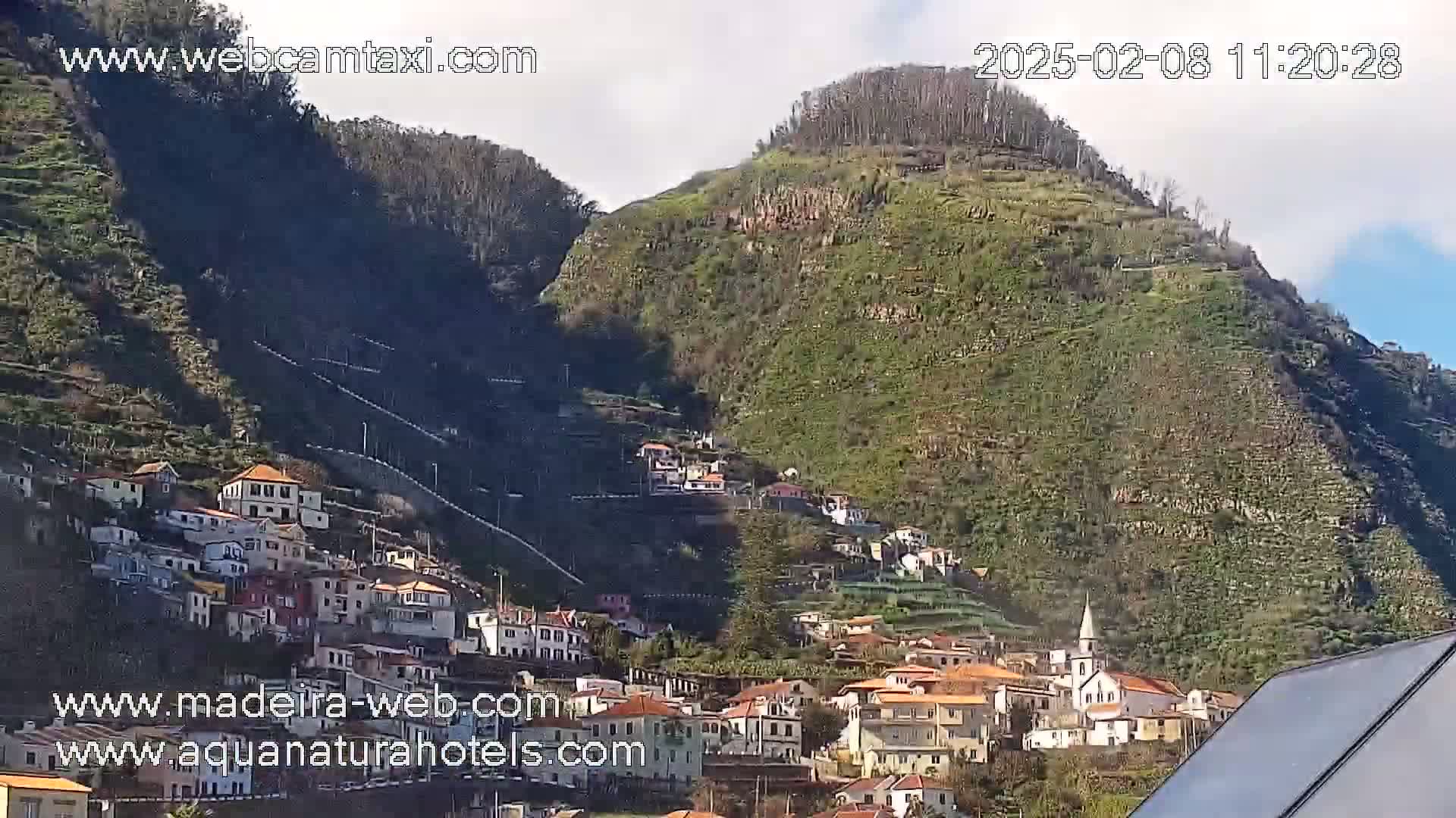 A hillside village nestled into a steep, terraced mountainside under a mostly clear sky.