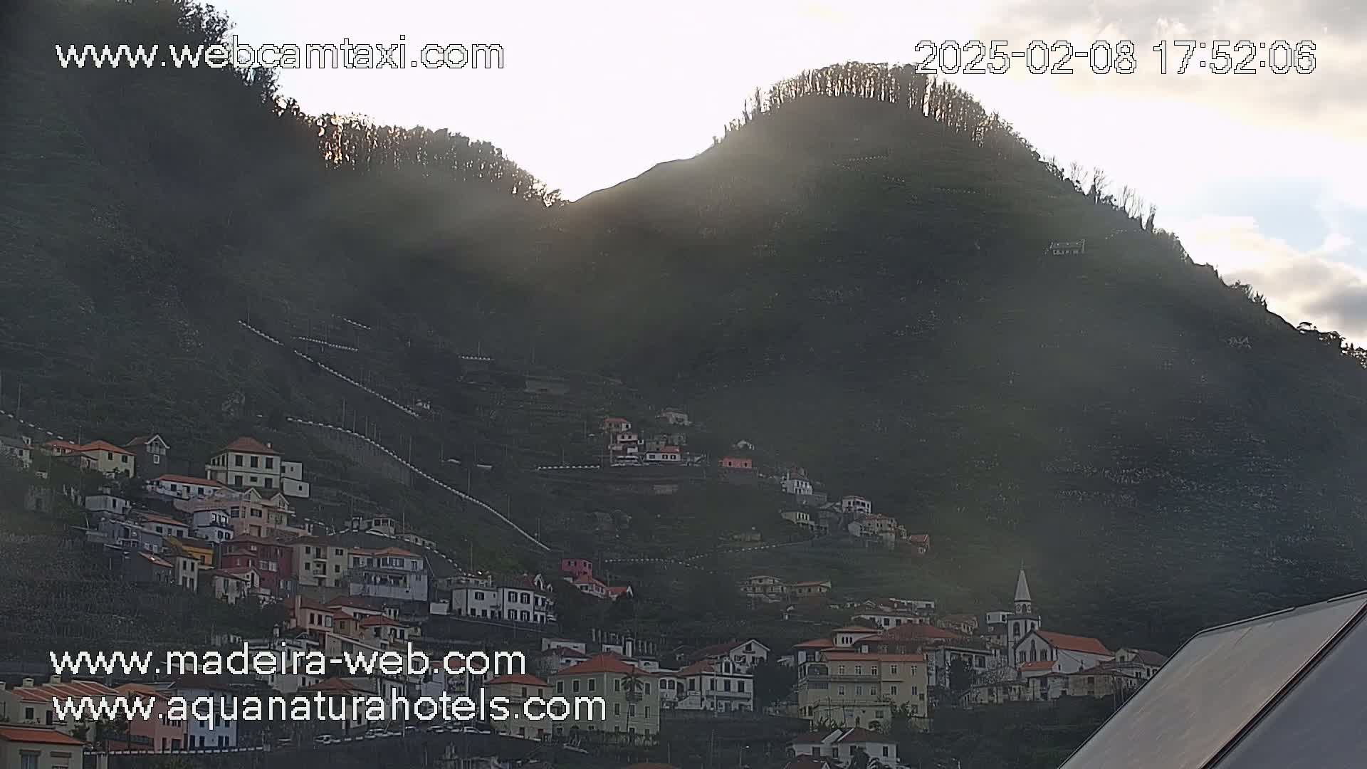 A village clings to the side of a sunlit, hazy mountain.