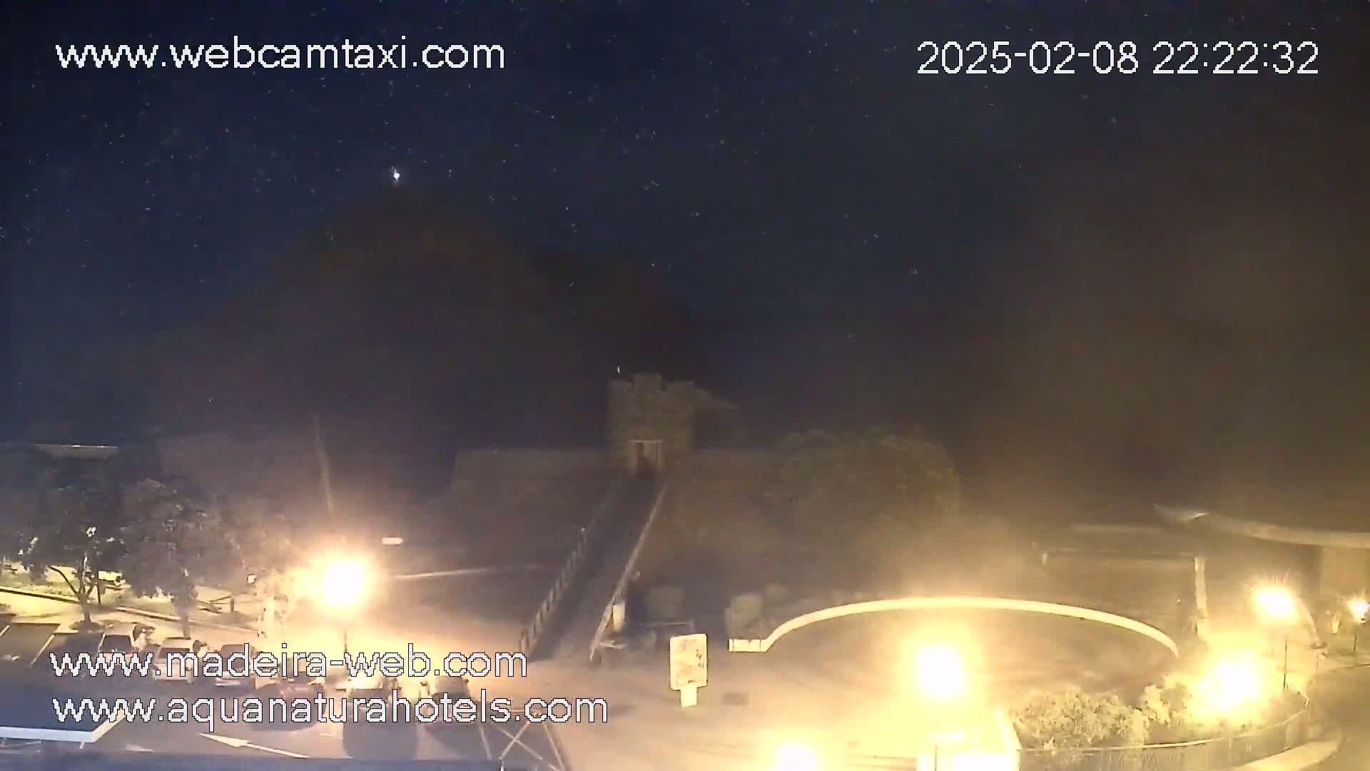 A nighttime outdoor scene shows a stone structure near a roadway with illuminated areas, under a clear, starry sky.