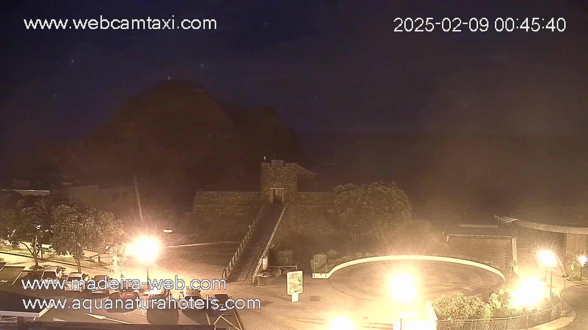 A nighttime view of a stone structure on a hill overlooking a dark, possibly hazy, ocean.