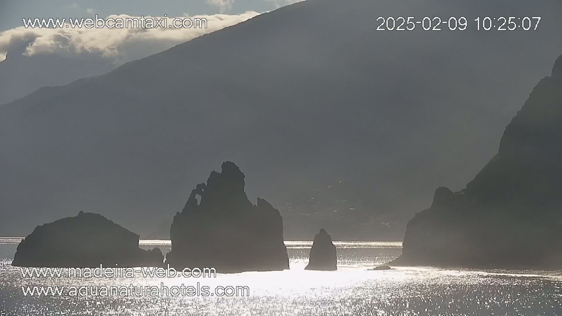 Dark, rocky coastal formations are partially silhouetted against a hazy, overcast sky, reflected in a calm body of water.