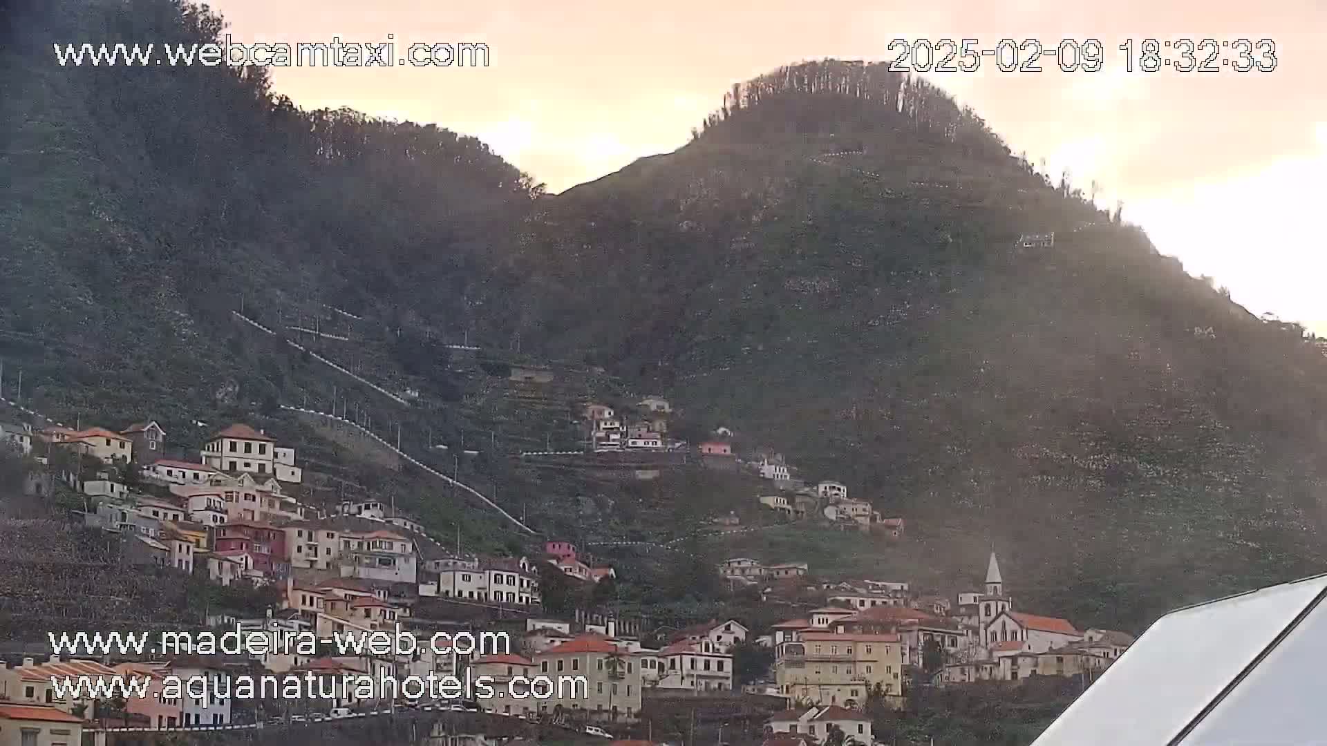 A hillside village nestled on a mountainside during a hazy, possibly dusty, sunset.