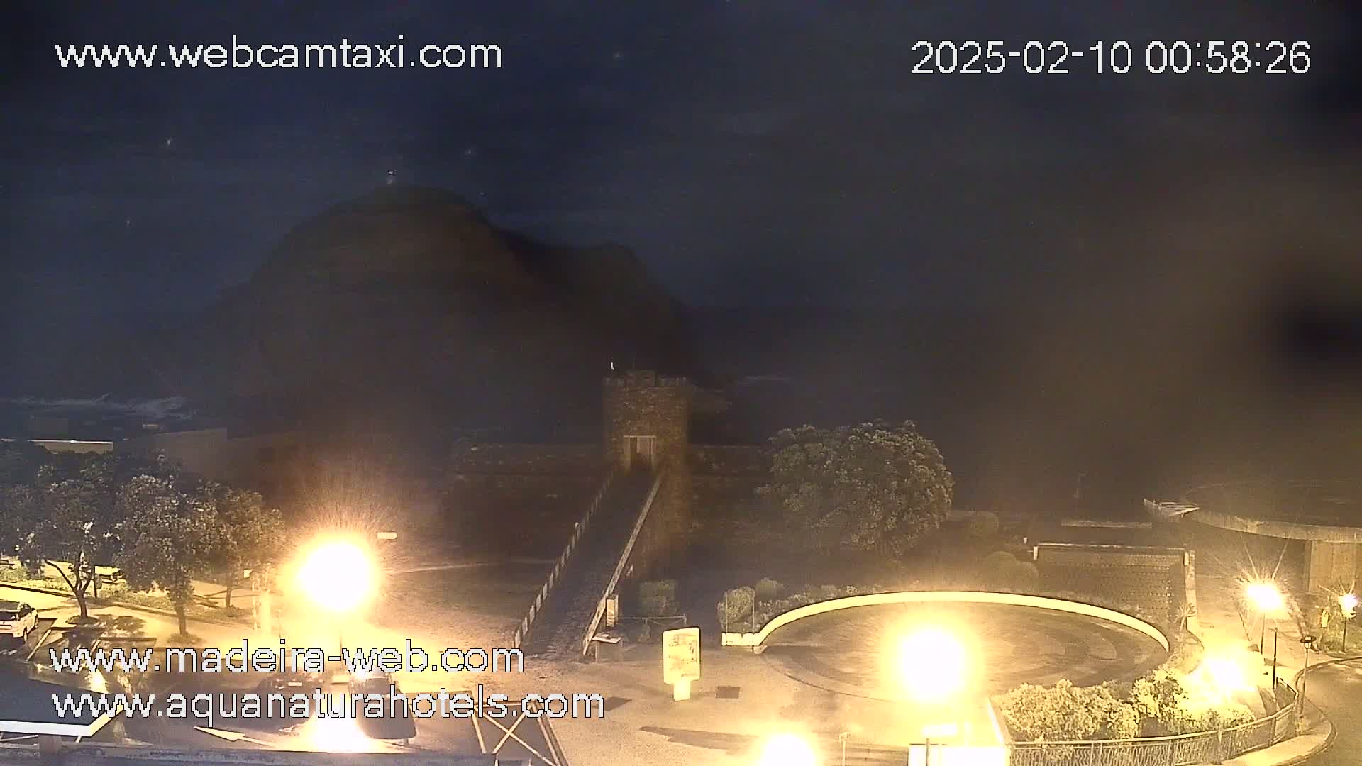 A nighttime view of a stone structure near a hill overlooking a dark body of water under a clear, dark sky.