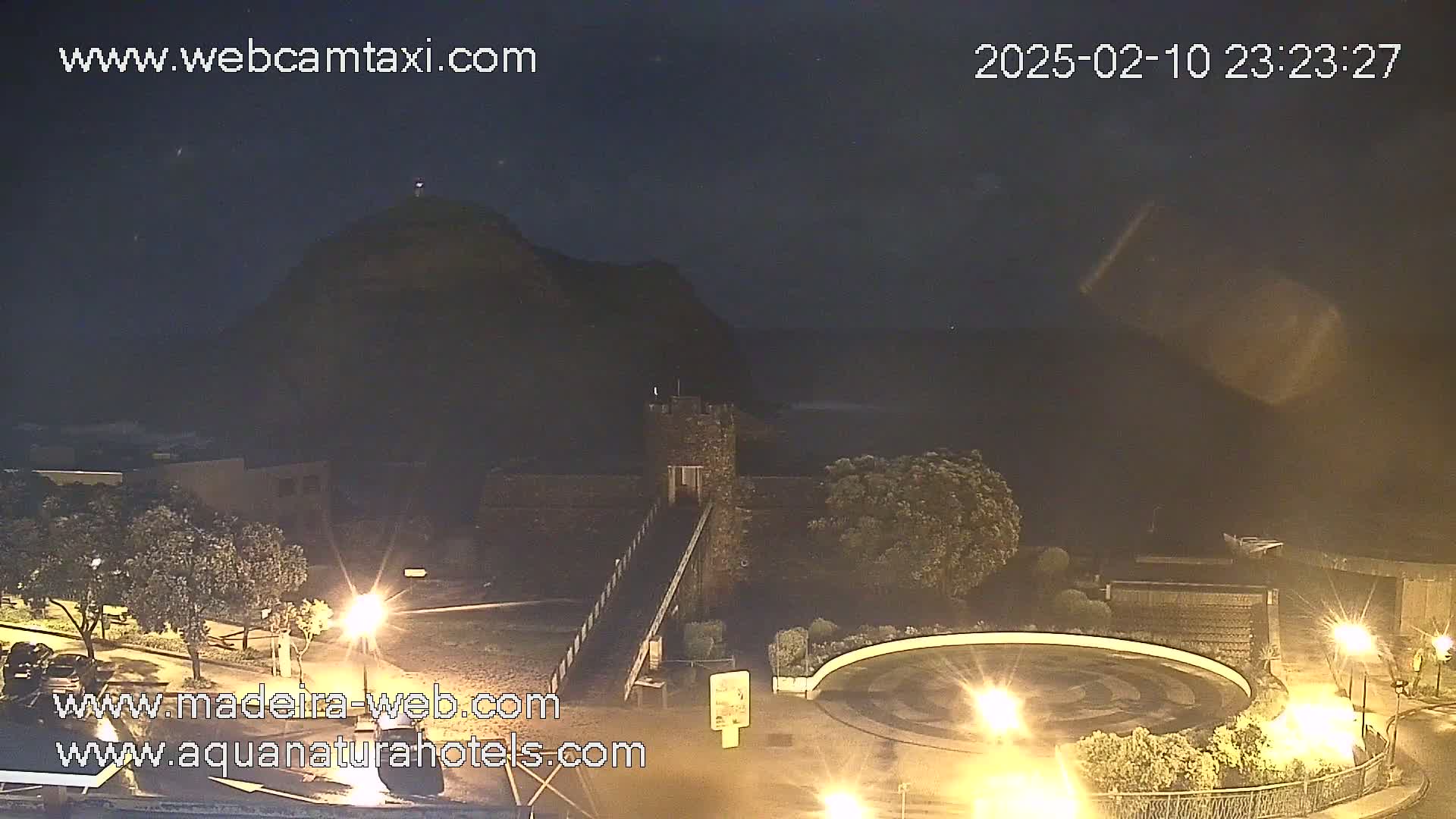 A nighttime view of a stone tower and a hill overlooking a wet, dark ocean under a cloudy sky.