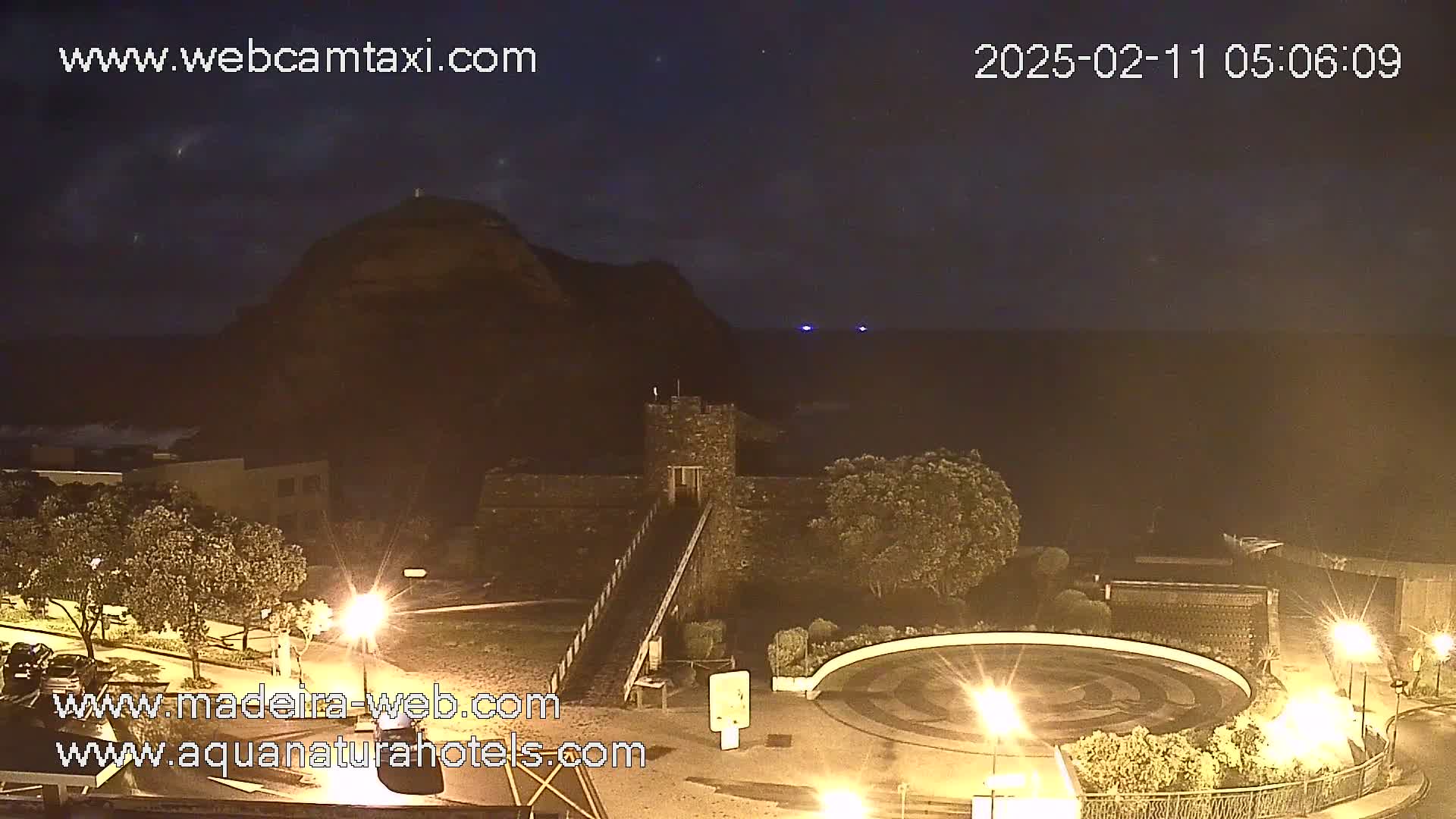 A nighttime coastal scene shows a stone structure near a hill overlooking a dark ocean under a clear, starry sky.