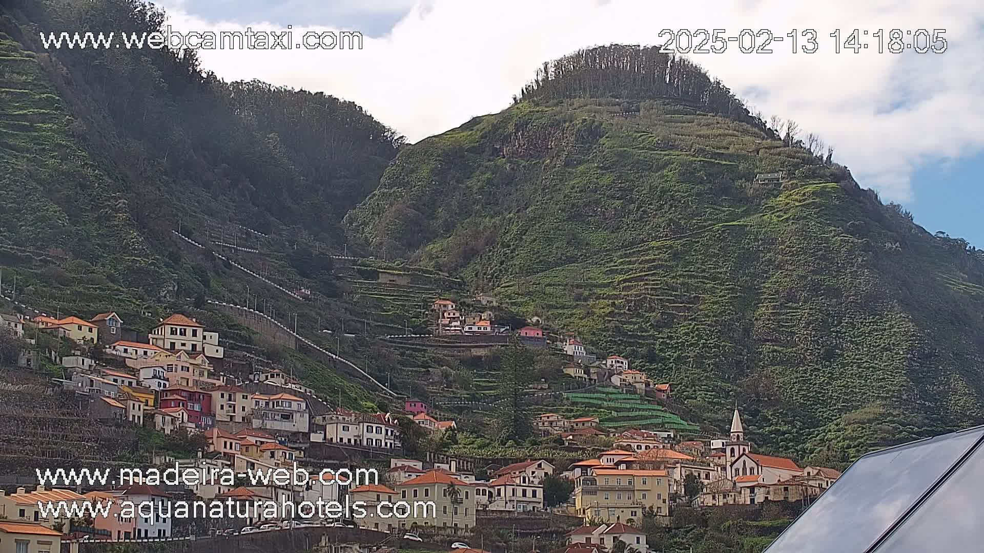 A village of colorful buildings climbs a terraced hillside under a partly cloudy sky.