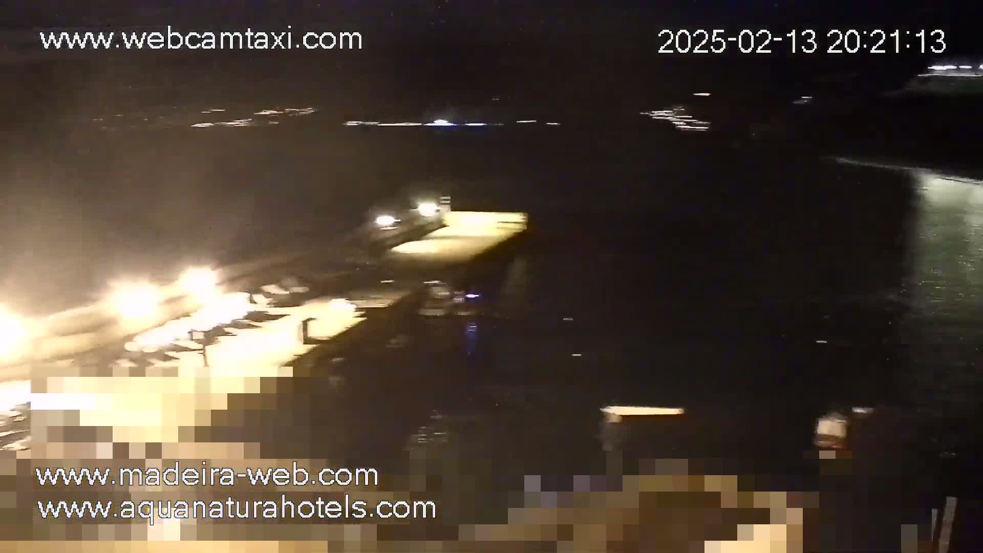 A nighttime, low-light view of a dark body of water next to a brightly lit dock or pier.