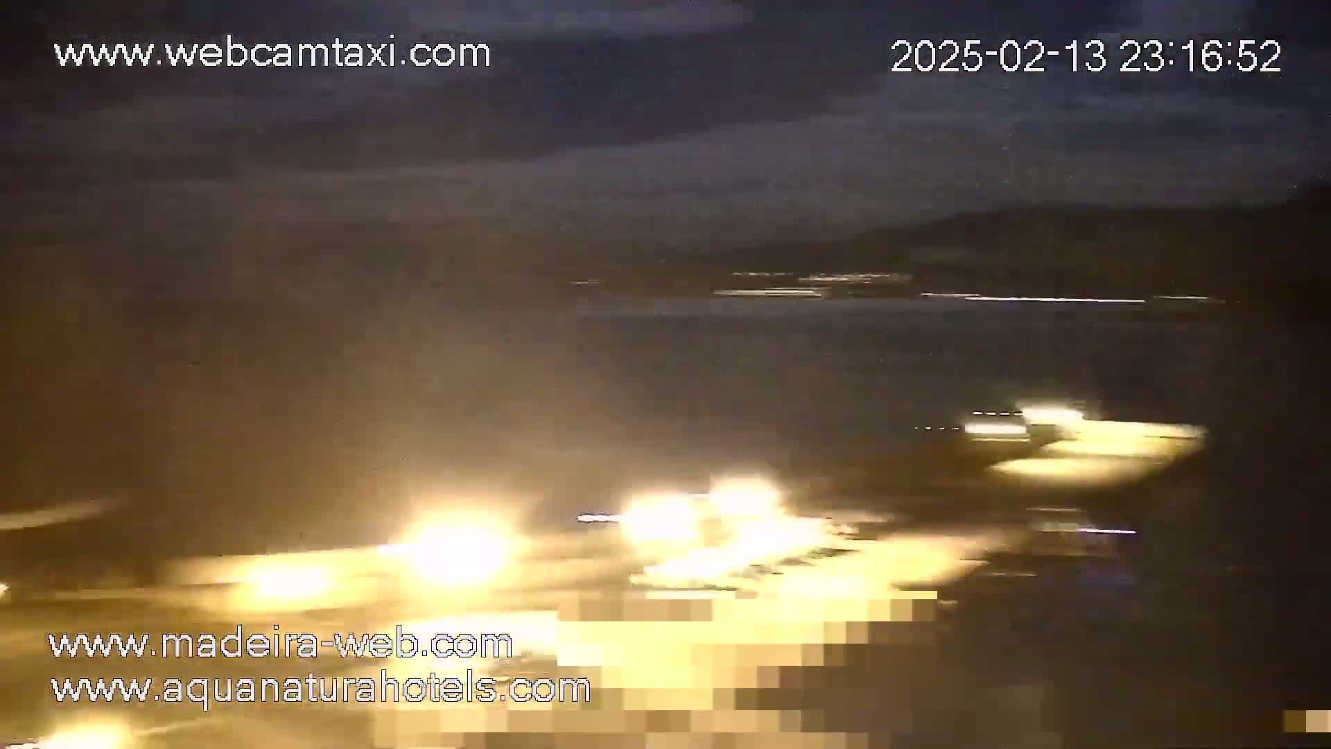 At night, under a dark cloudy sky, bright headlights of vehicles are visible on a road.