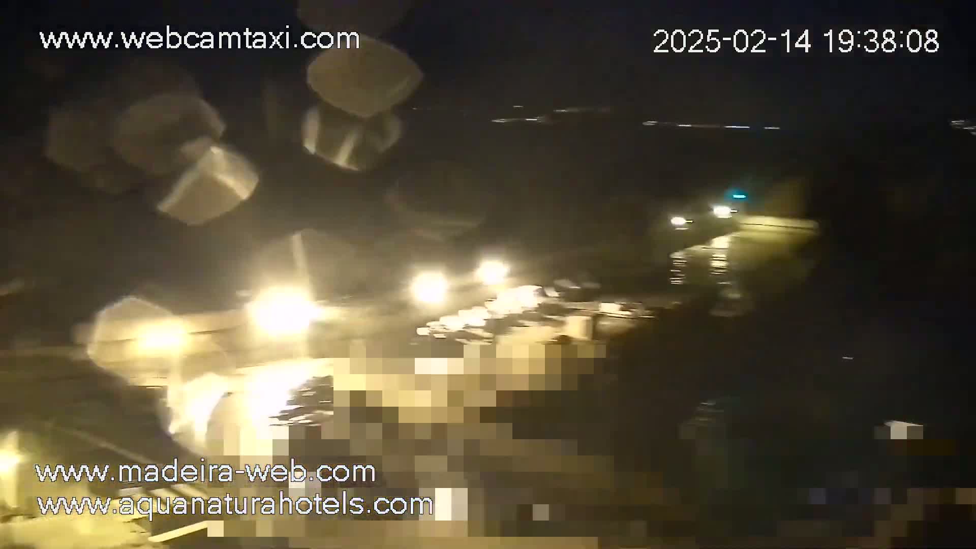 A nighttime, blurry view of traffic on a wet road, illuminated by headlights and streetlights.