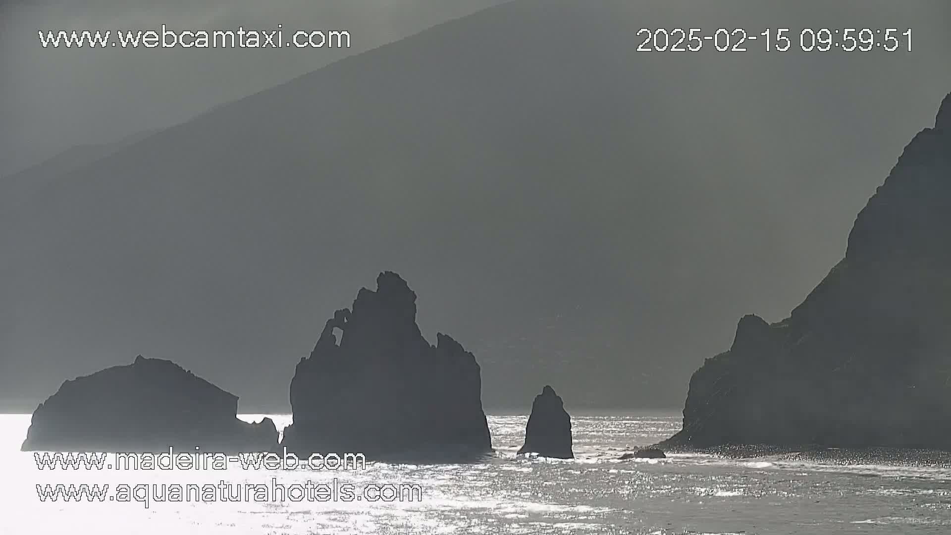 Dark, silhouetted rock formations rise from a slightly choppy sea under an overcast sky.