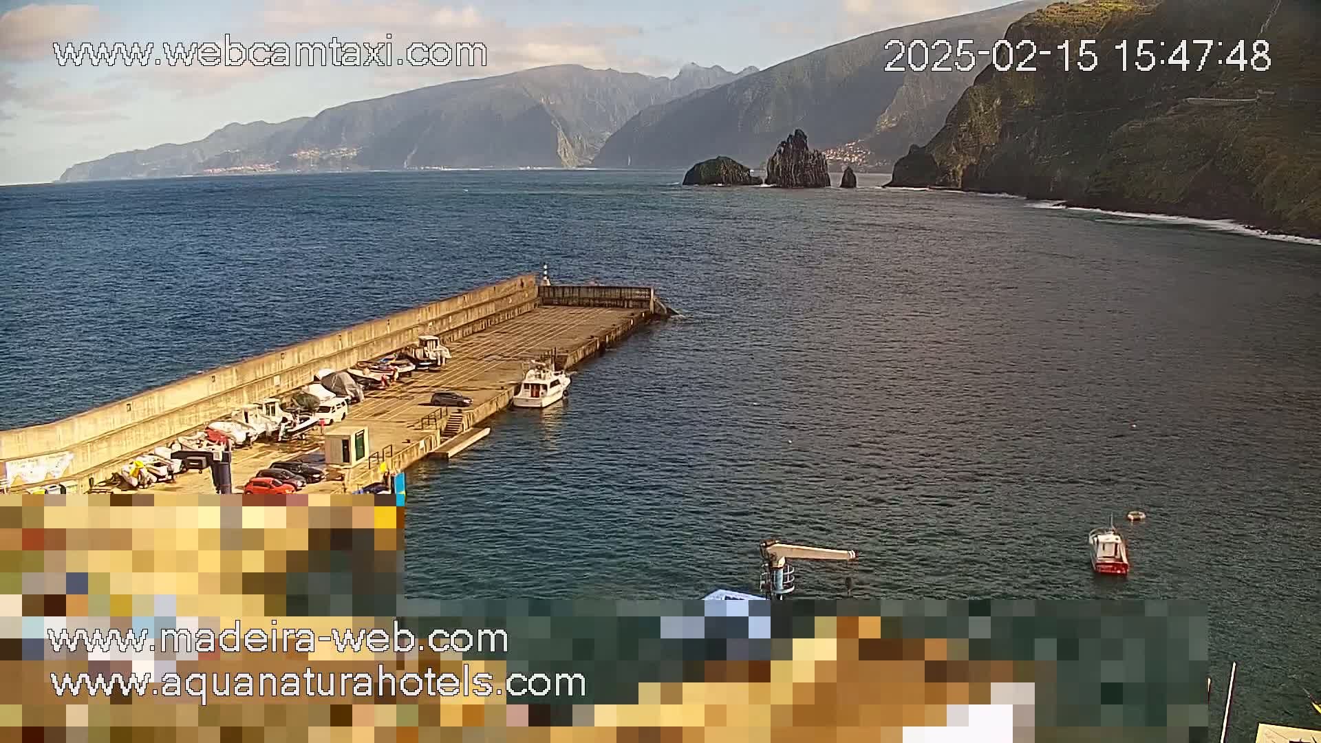 A small harbor with several boats is situated near a rocky coastline under a partly cloudy sky.