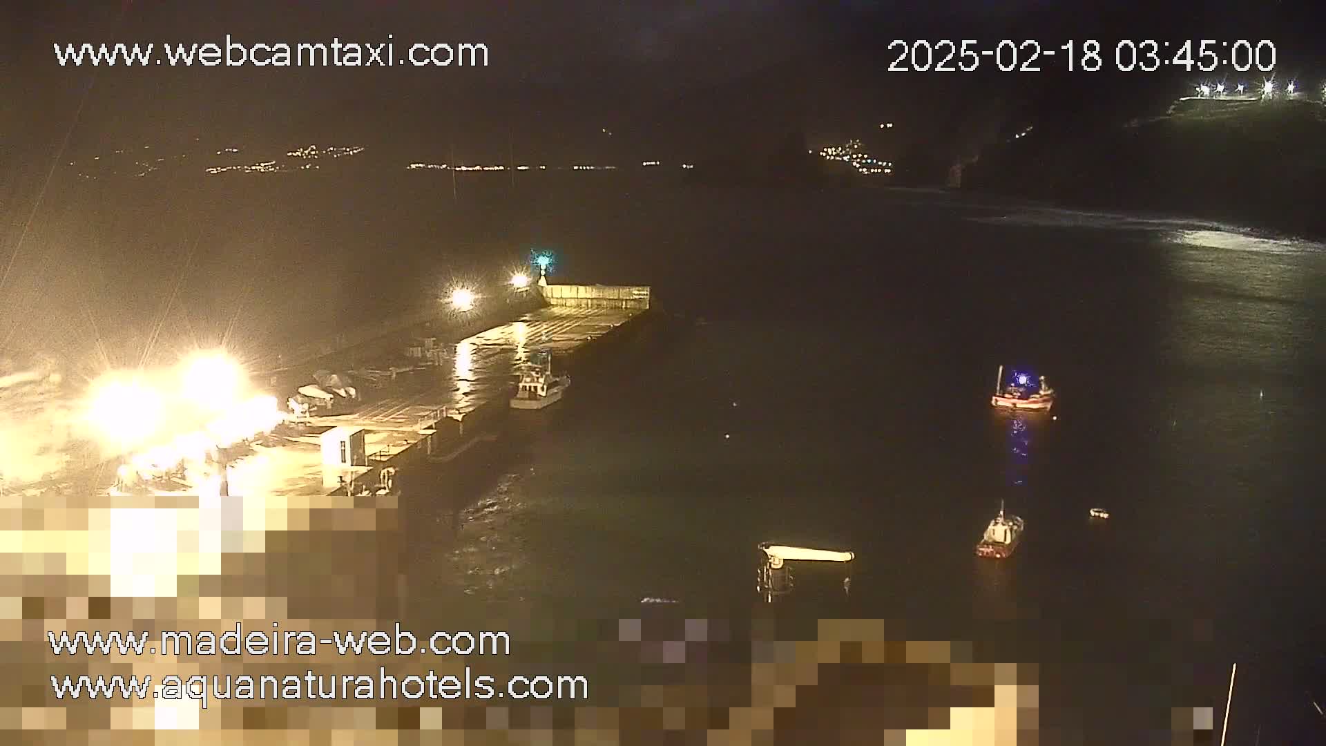 A nighttime, low-light view of a harbor with several small boats and a pier, with some lights illuminating the scene.