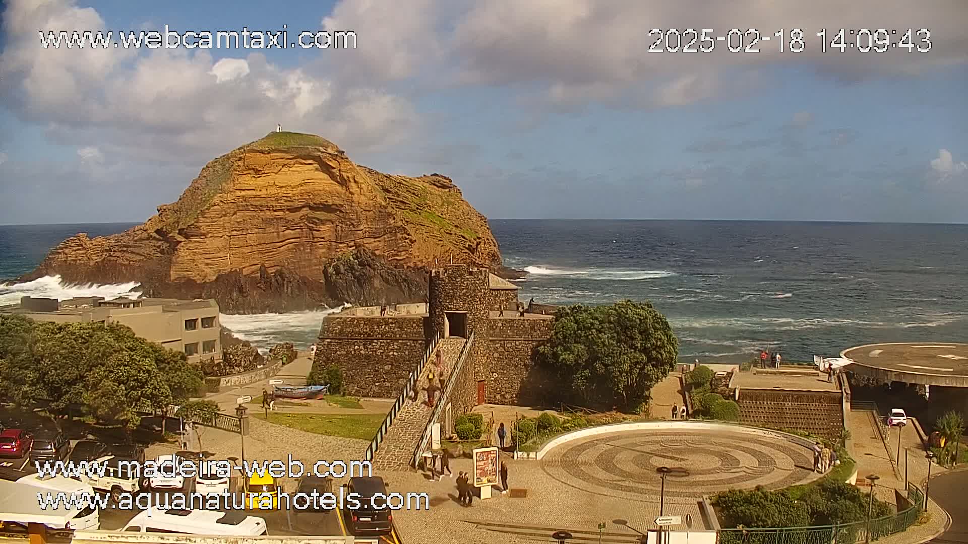 A stone fort and a rocky island are situated on a coast with a partly cloudy sky and a somewhat choppy ocean.
