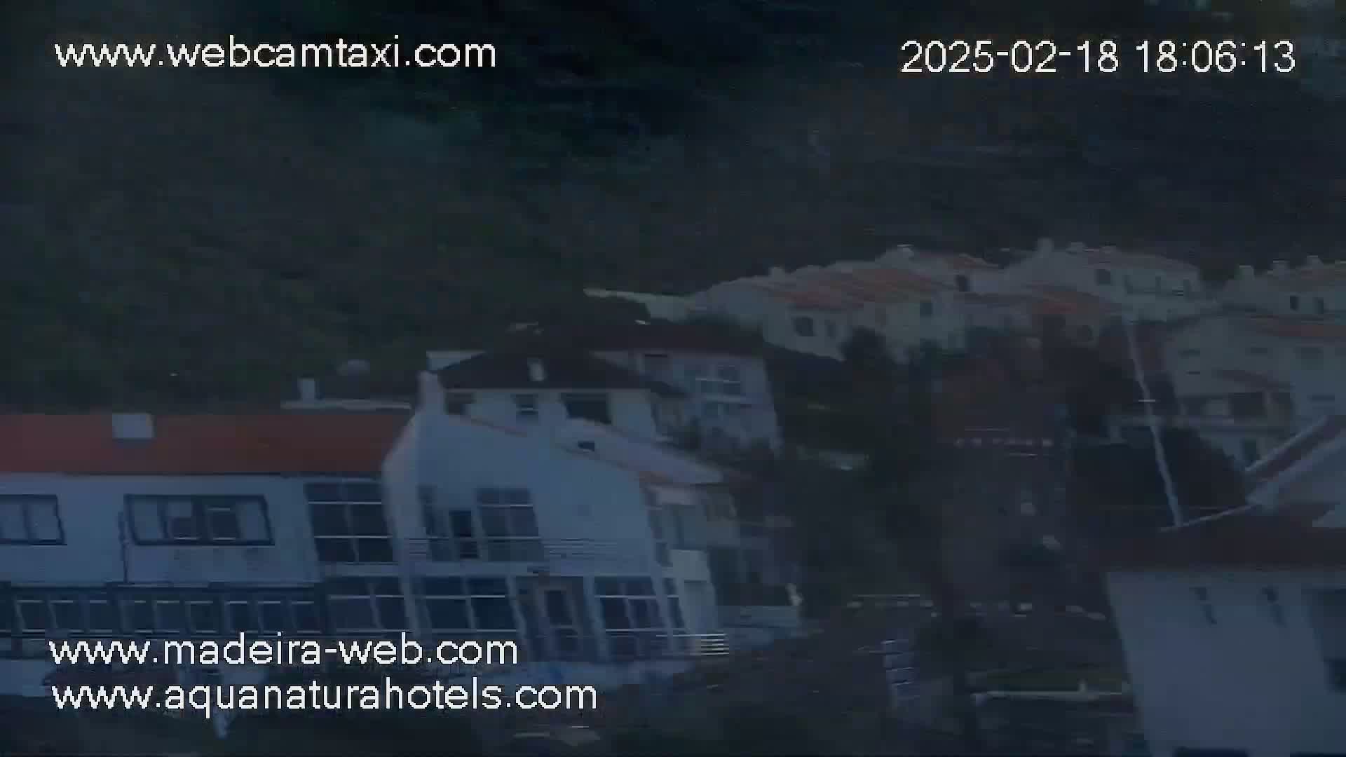 A nighttime view of a hillside town with multiple buildings, appearing somewhat blurry in low-light conditions.