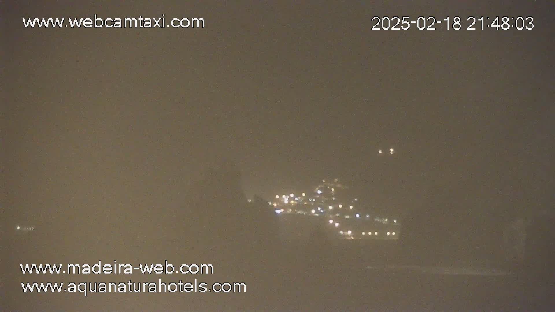A hazy night scene shows a distant cluster of lights nestled in a hill, possibly a town or village.