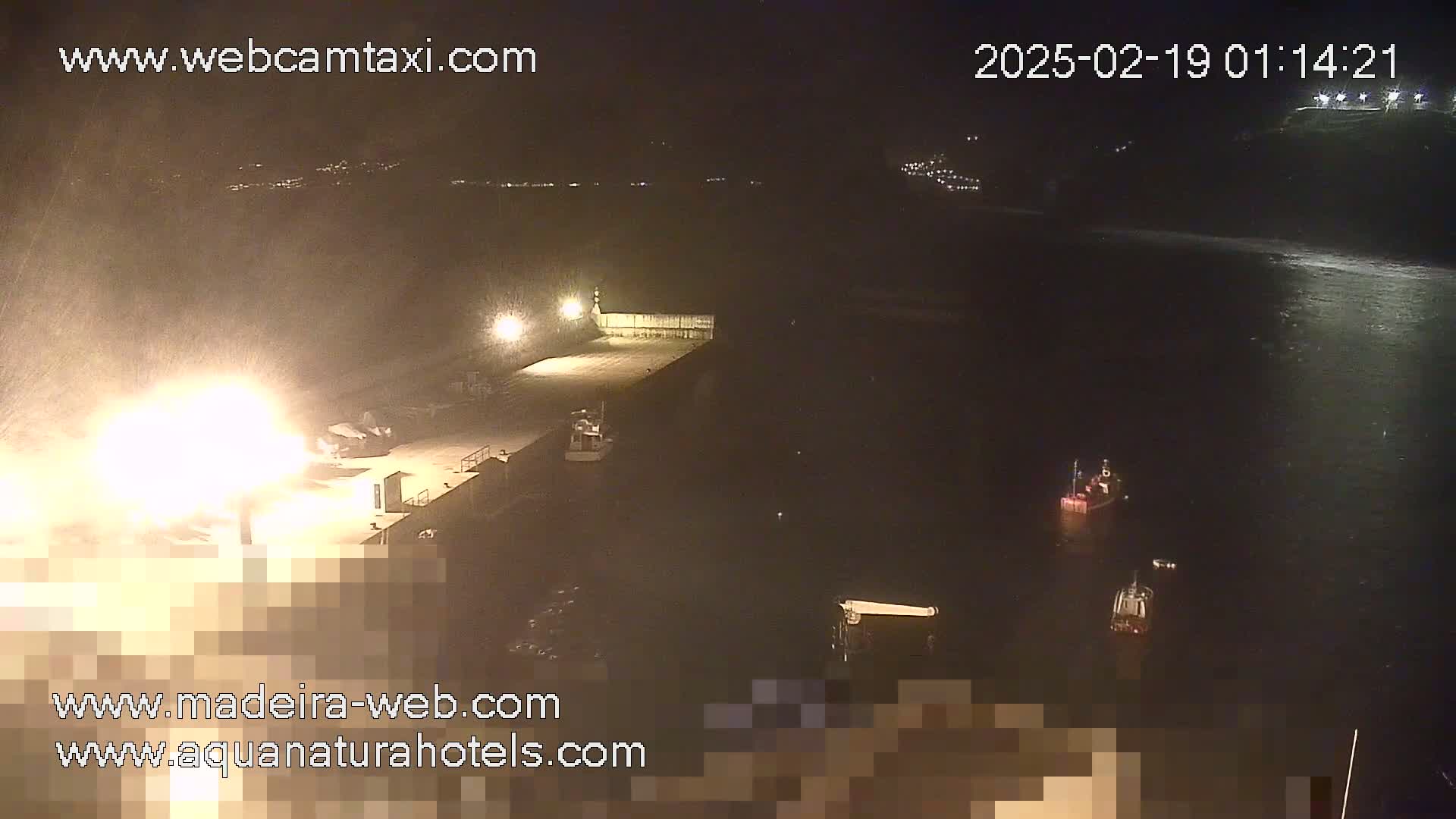 A nighttime view of a harbor with several small boats in the water under snowy conditions.