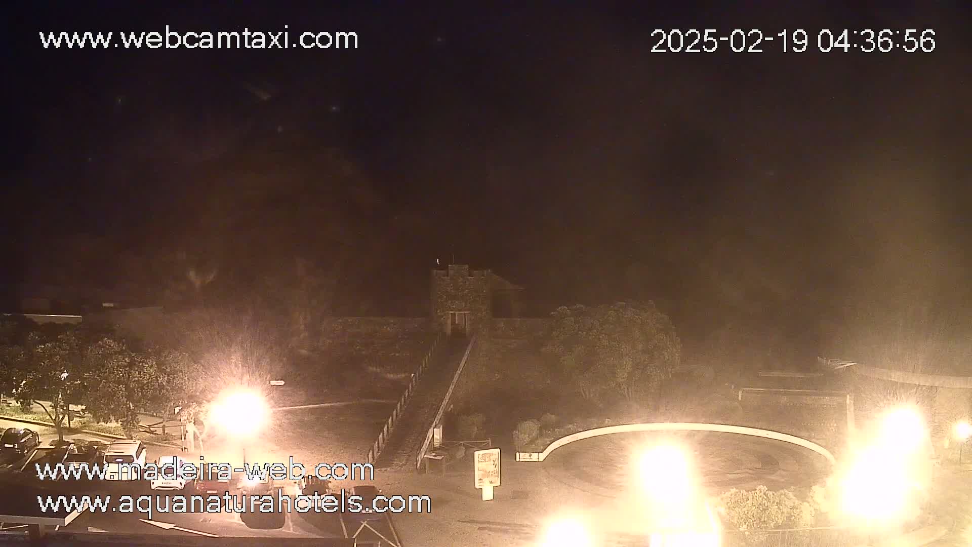 A nighttime view of a stone structure, possibly a tower, with a paved area and bright lights, under hazy or foggy conditions.