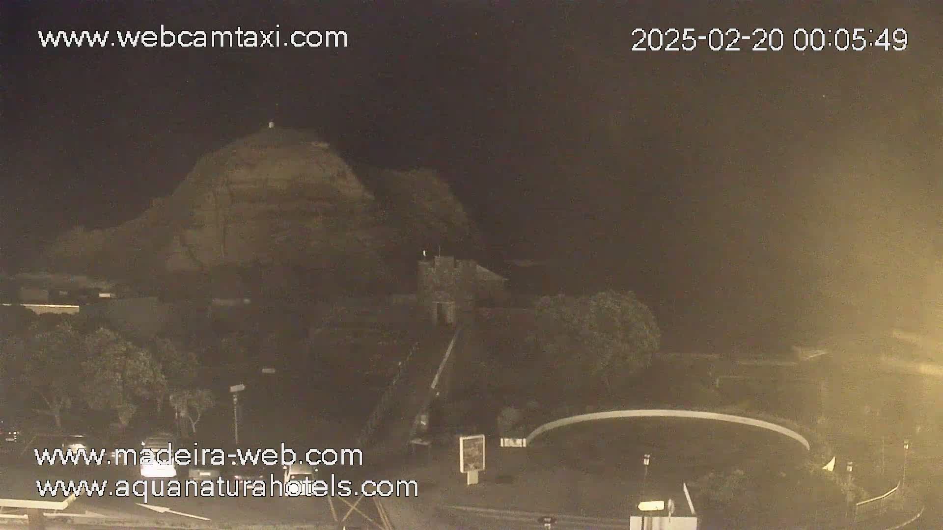 A nighttime, long shot of a rocky hill and surrounding landscape, possibly near a roadway.
