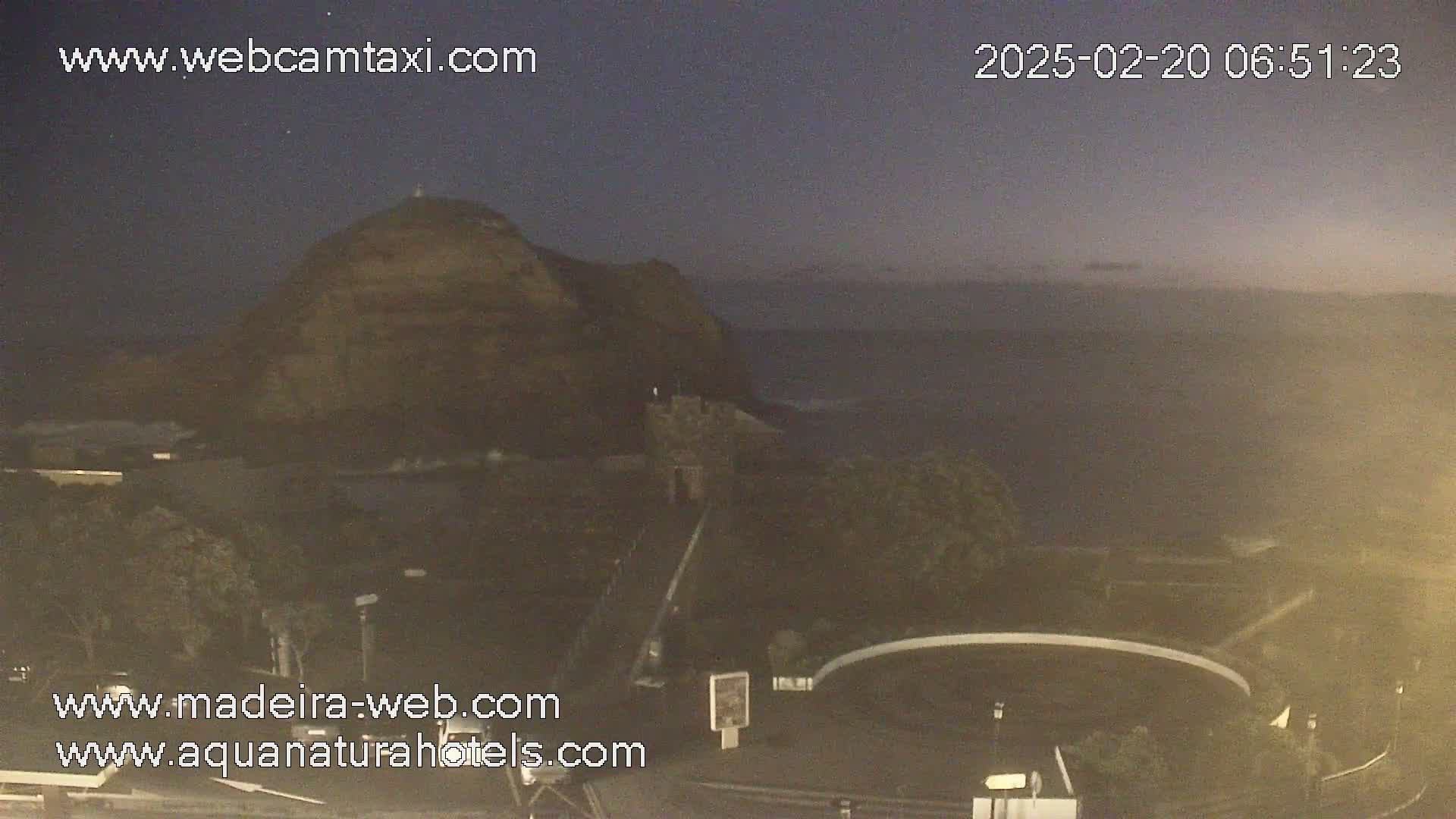 A dark, rocky hill overlooks a calm, dark ocean under a twilight sky.