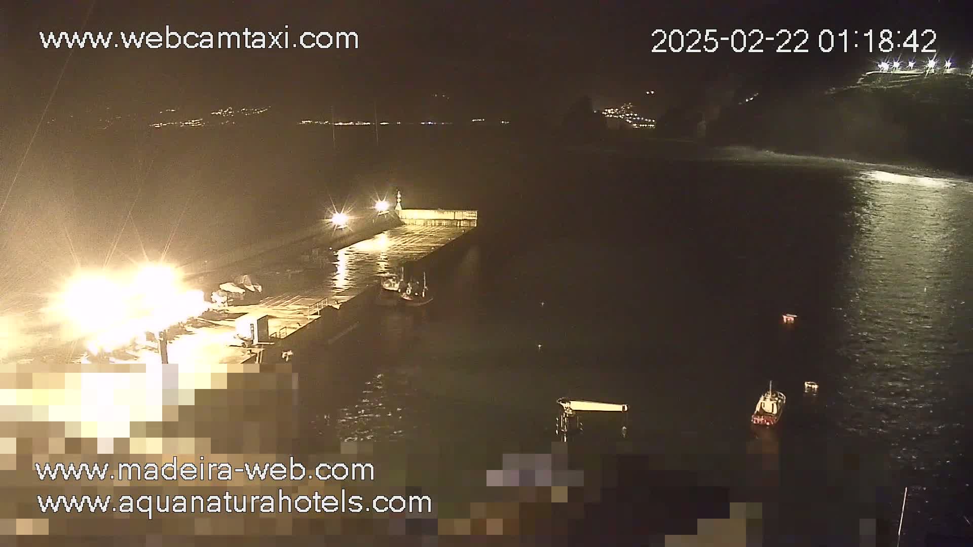 A nighttime, aerial view shows a pier with several boats moored alongside it, in somewhat choppy water.