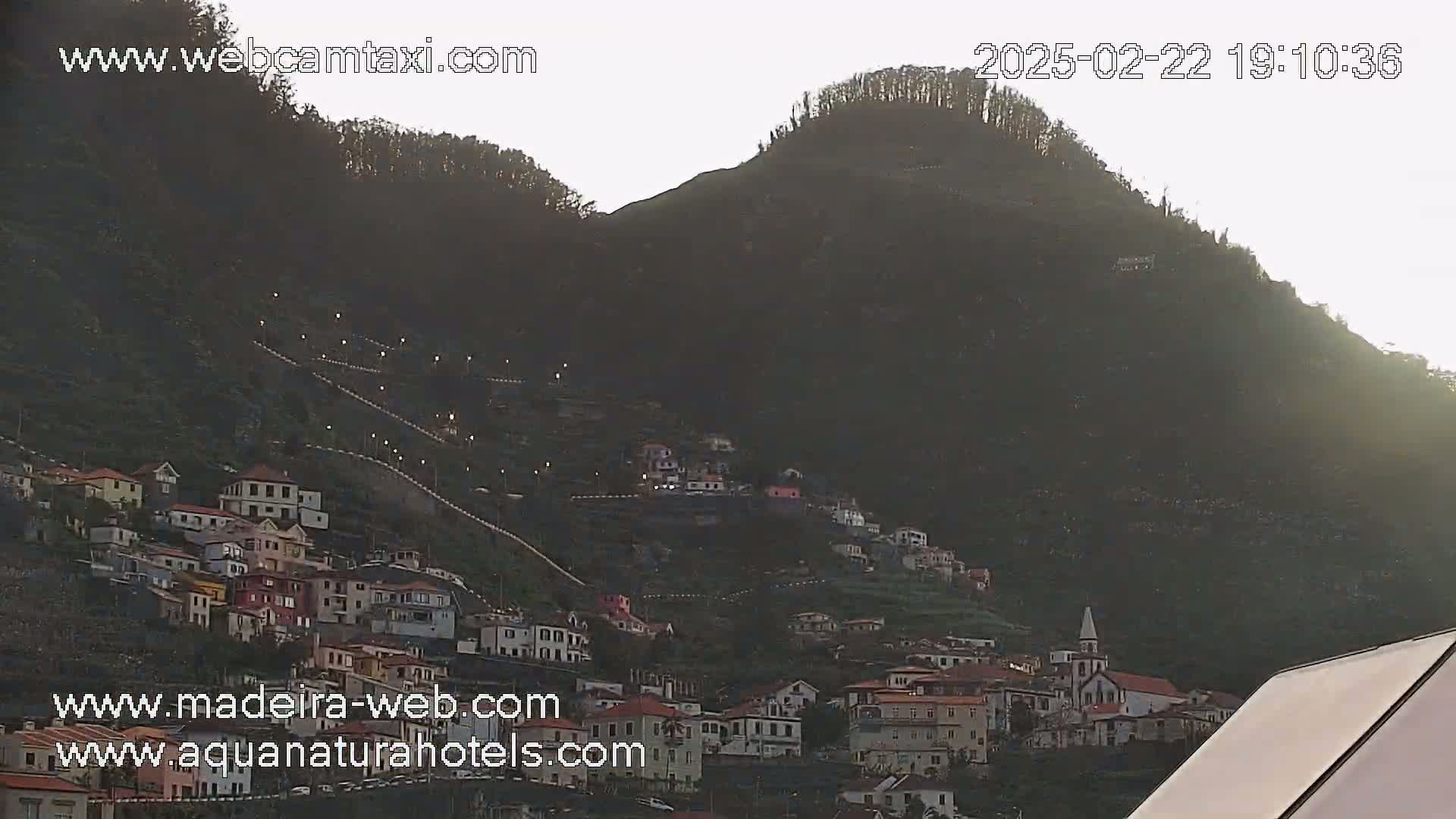 A hillside village is nestled on a mountainside at dusk, with a lighted pathway winding upward.