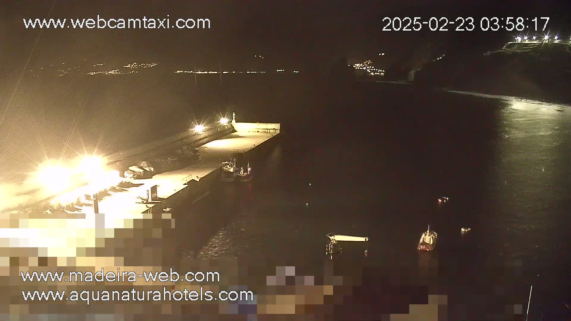 A nighttime view of a harbor with several boats near a lit-up pier, under calm water conditions.