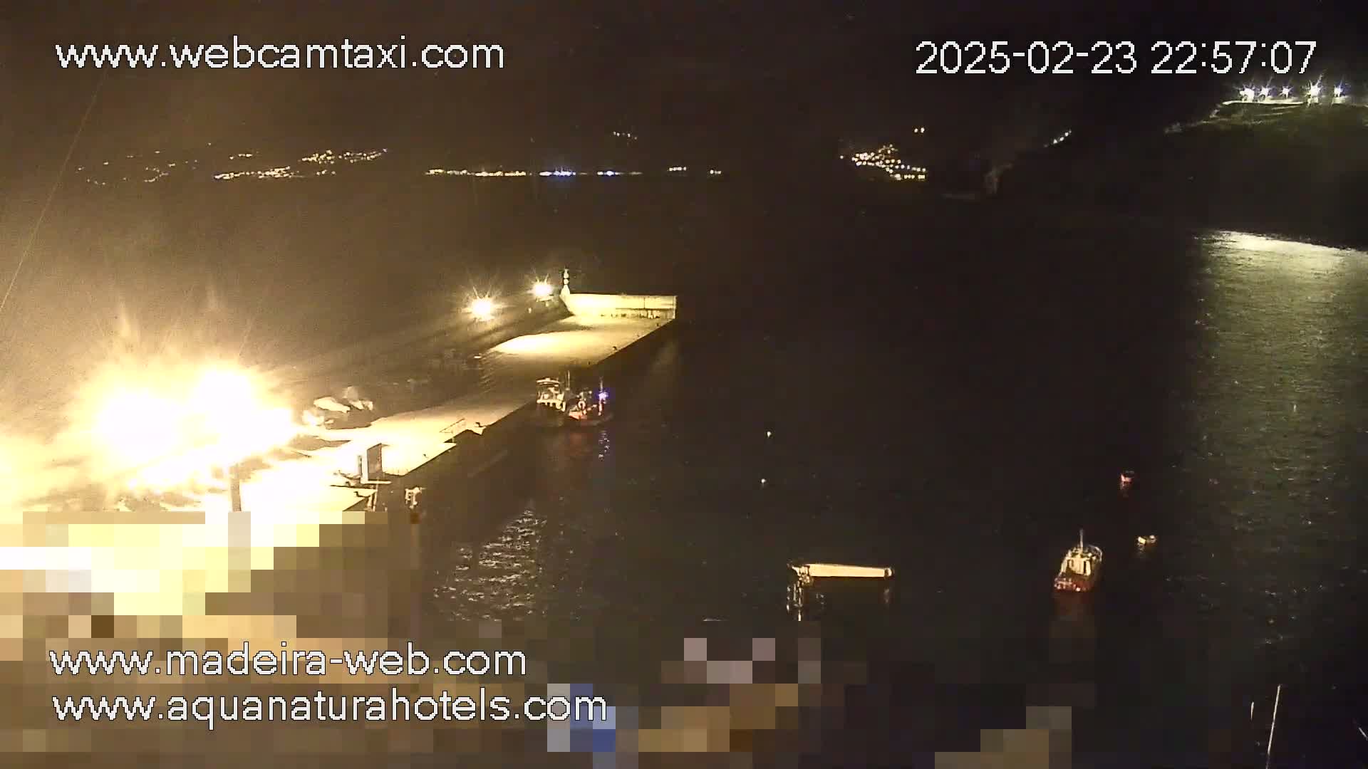 A nighttime, aerial view of a harbor with several small boats in the water near a brightly lit dock.