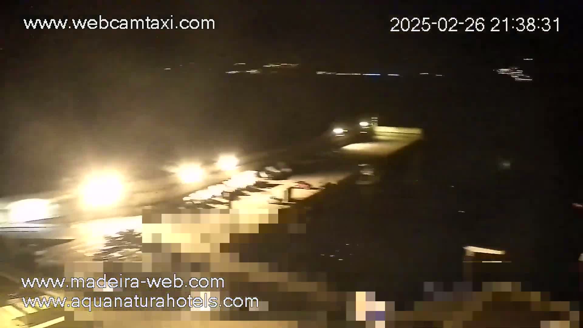 A nighttime, blurry view of a waterfront area with vehicles and lights visible under hazy or foggy conditions.