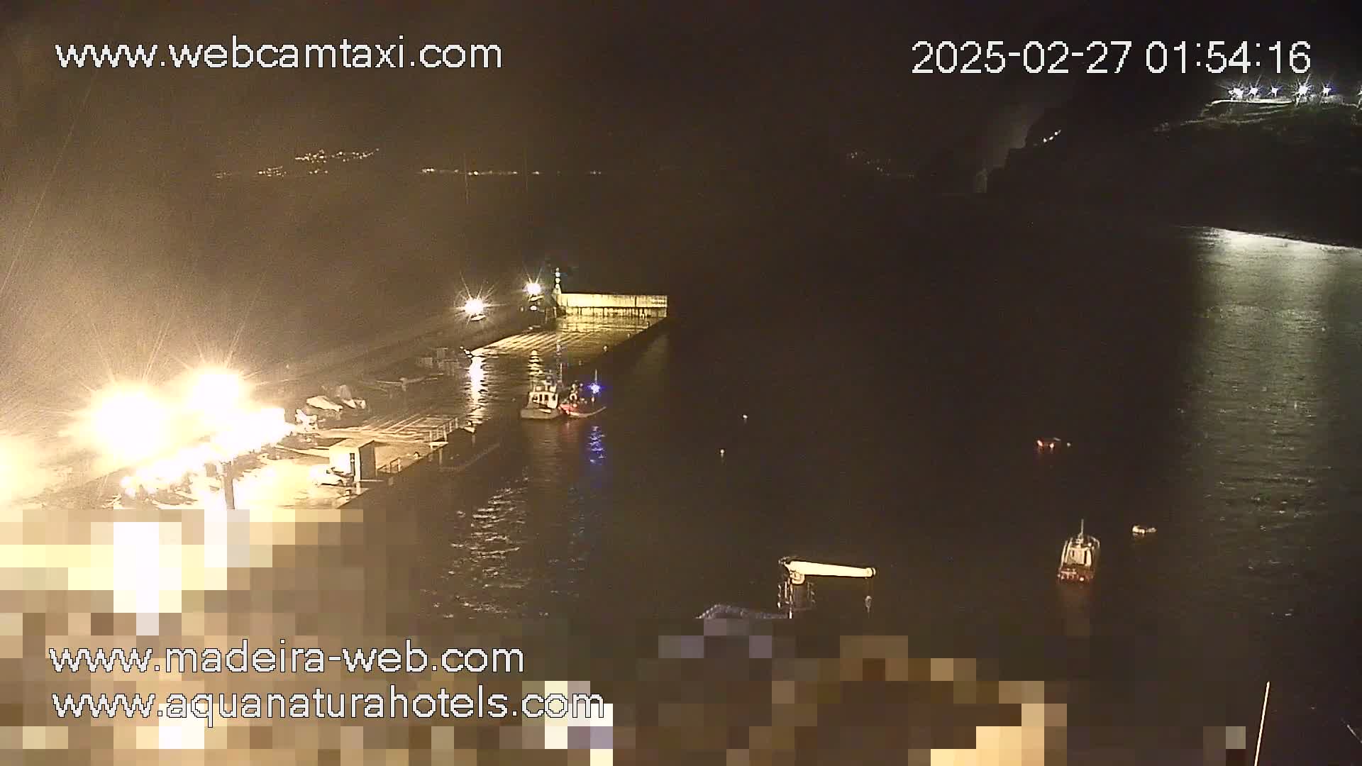 A nighttime, dimly lit harbor scene shows a small boat near a dock with lights on, and another boat further out in dark water.