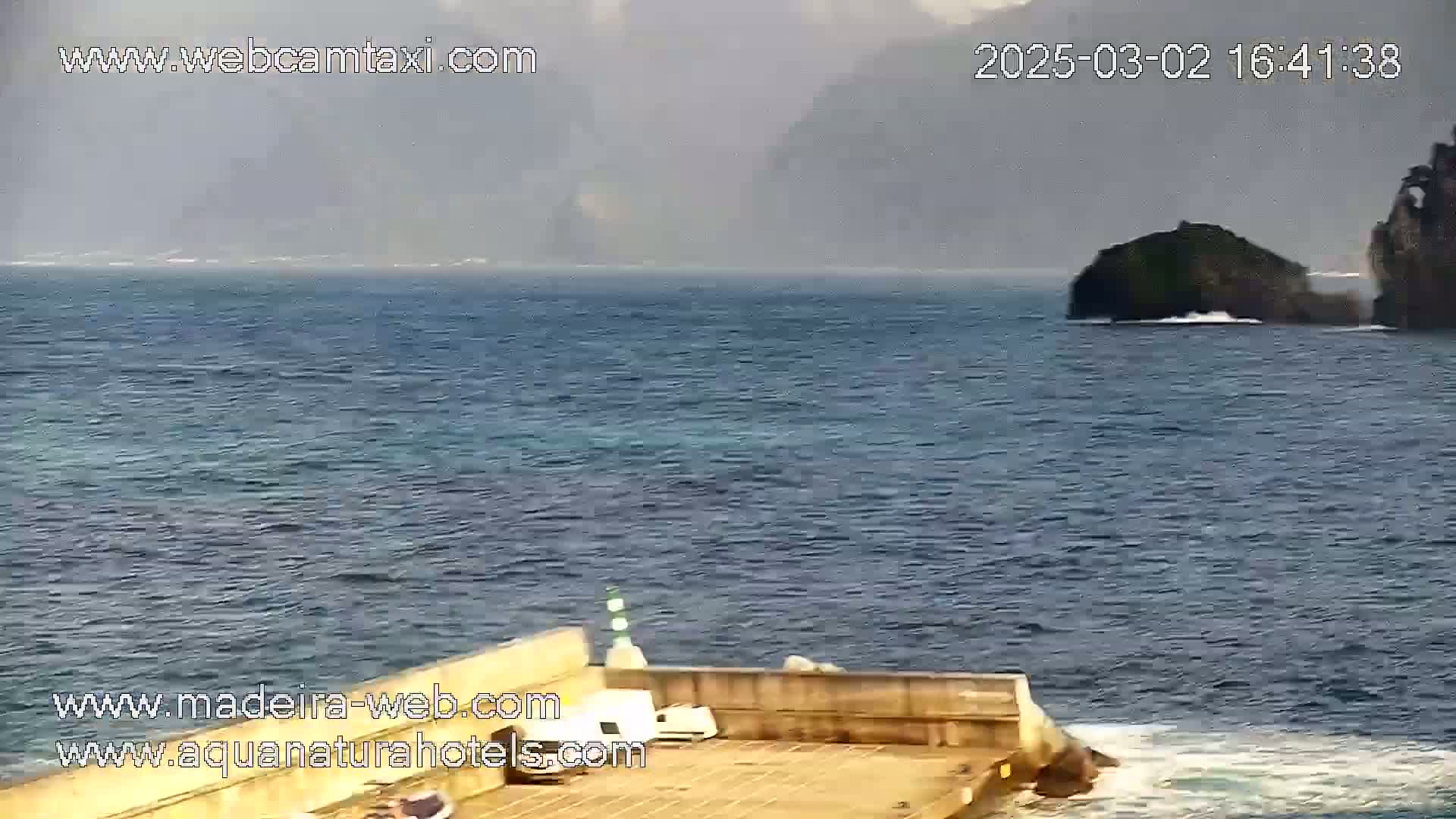 A view from atop a dock shows a dark, somewhat overcast day at sea with a rocky outcropping in the distance.
