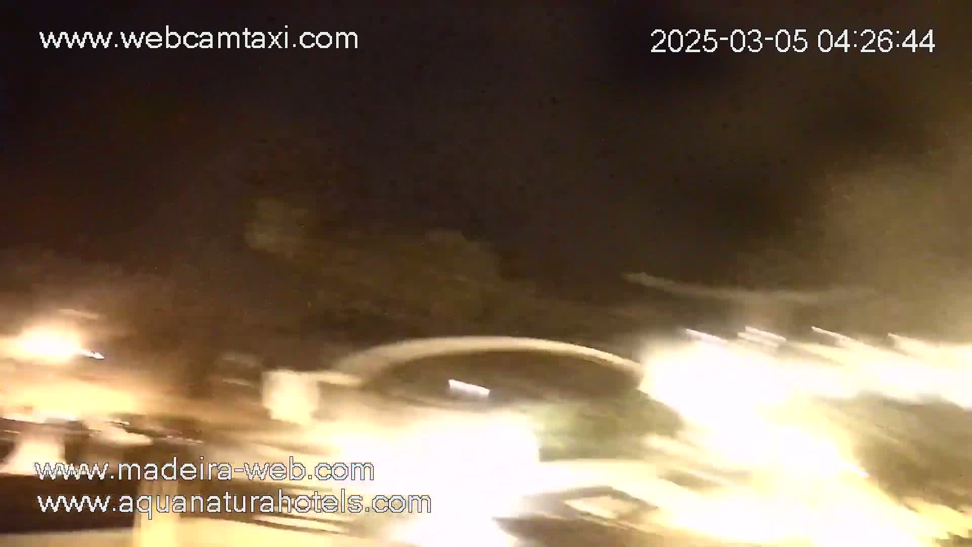A nighttime, blurry image shows bright headlights of moving vehicles on a road under a dark sky.