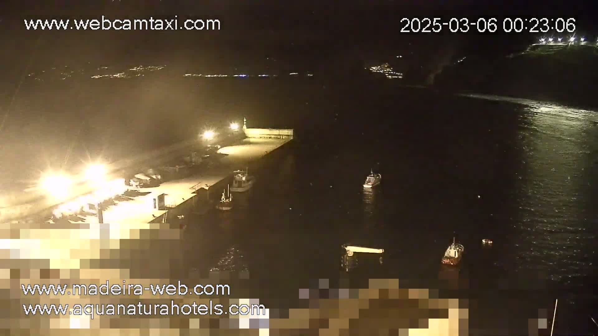 A nighttime, aerial view of a harbor with several boats docked and in the water, illuminated by artificial lights.