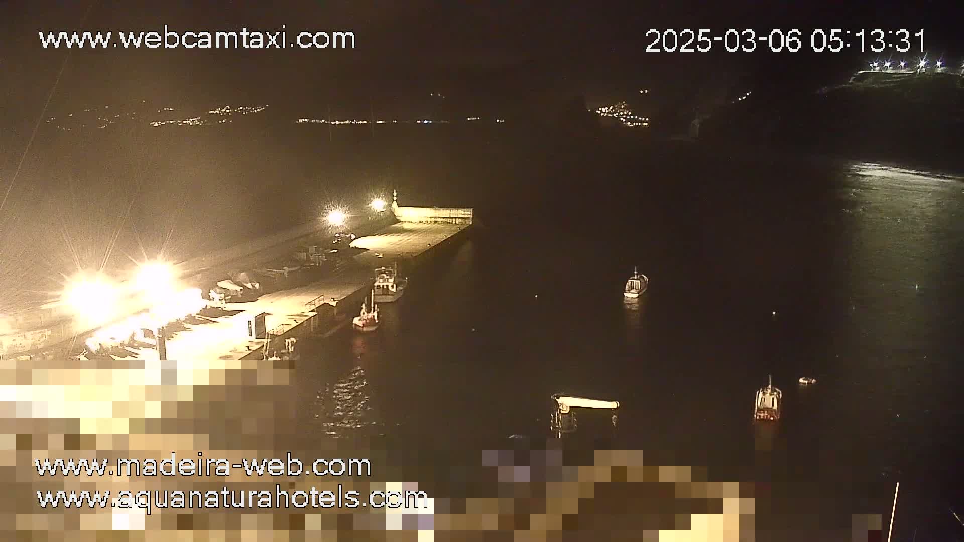 A nighttime view of a harbor with several boats moored at a pier, under dark, calm conditions.
