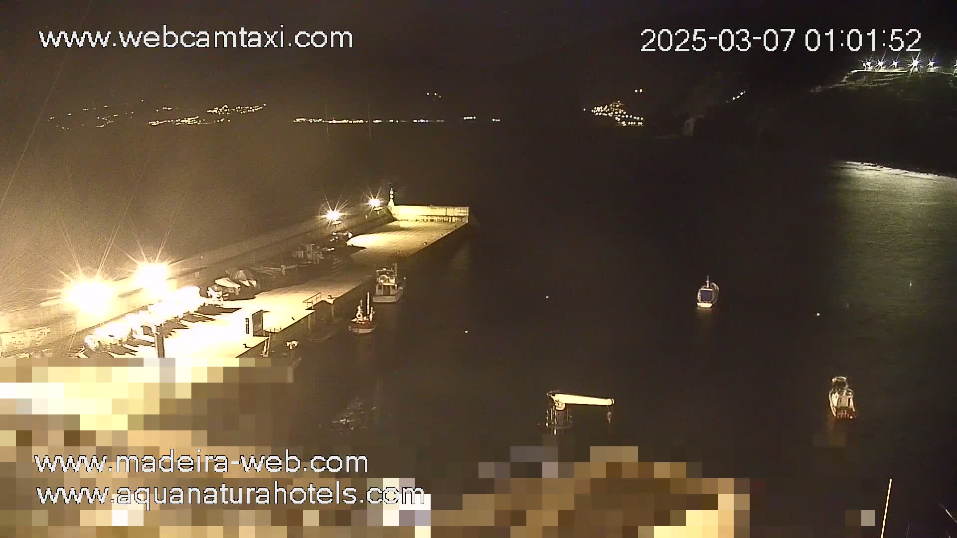 A nighttime, high-angle view of a harbor with several boats moored at a brightly lit dock, under a dark sky.