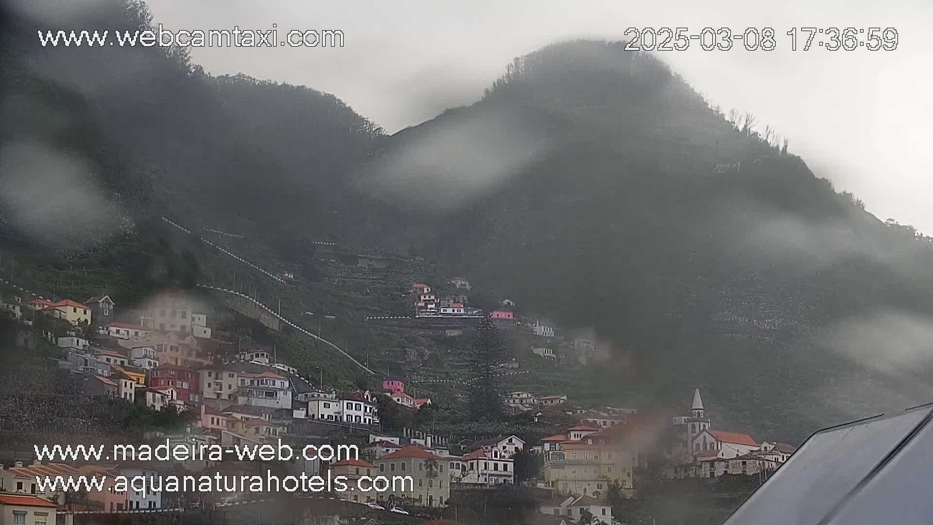 A rain-swept village clings to the slopes of a misty, verdant mountain.