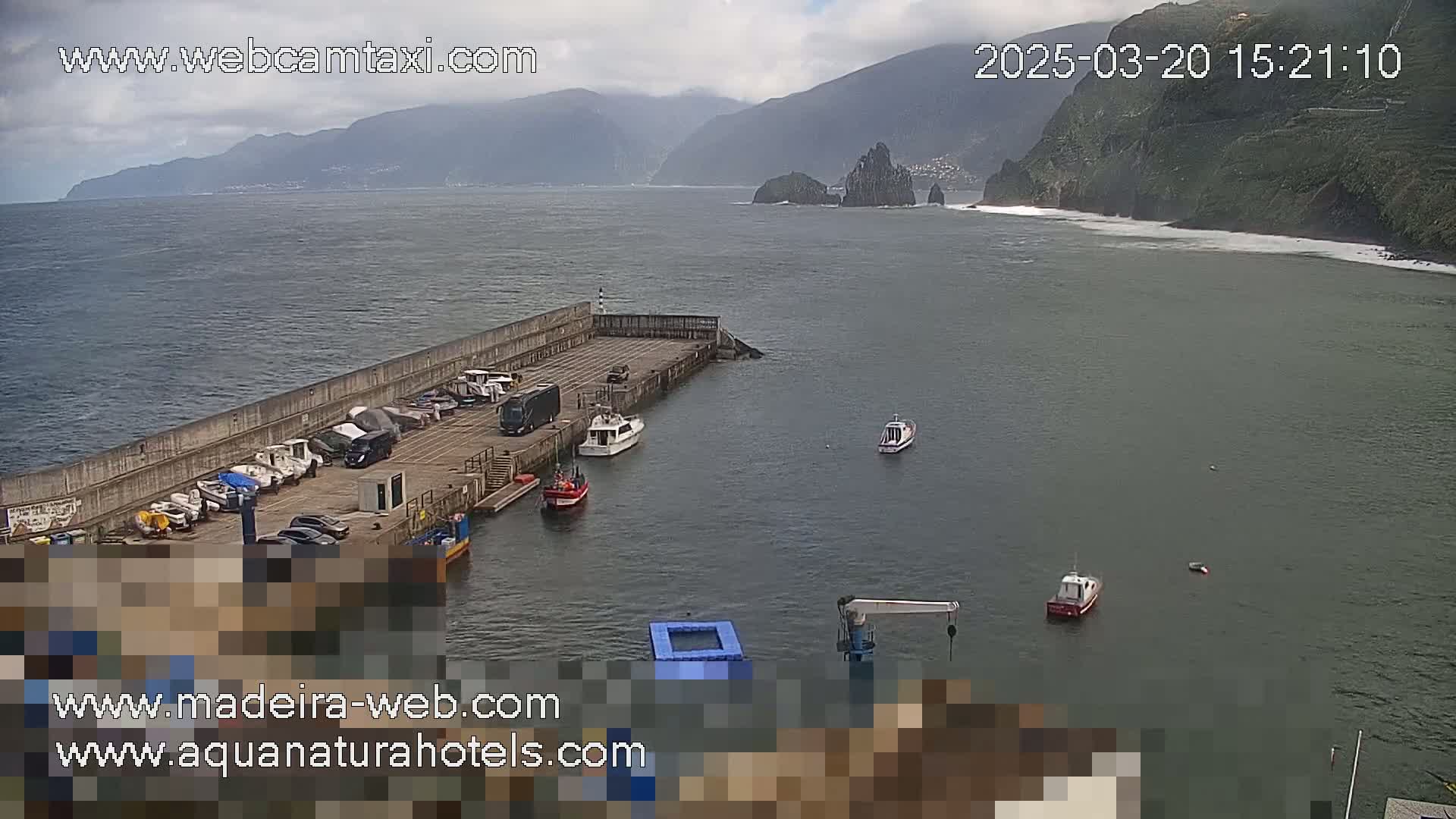 A small harbor with several boats is nestled next to a rocky coastline under a partly cloudy sky.