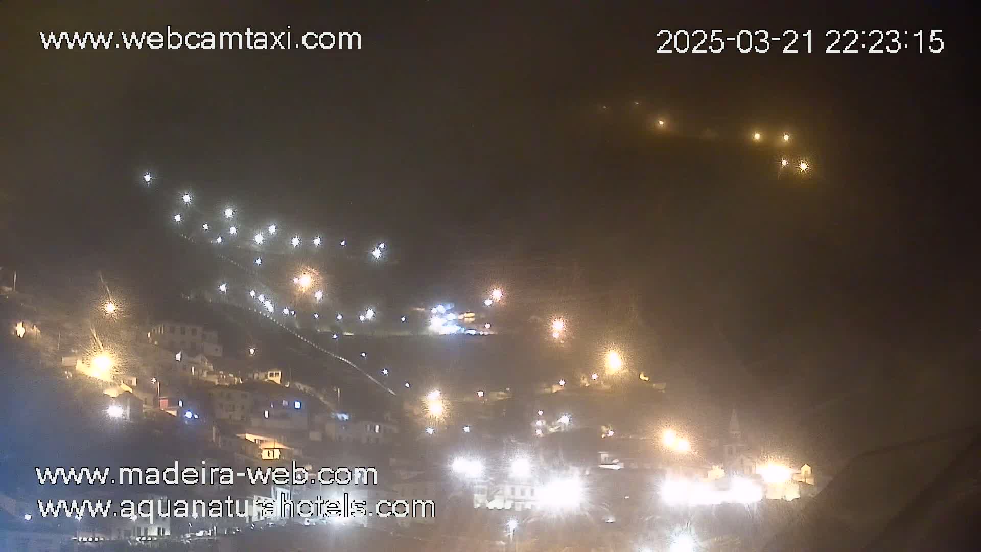 A hillside town at night is illuminated by numerous lights in foggy conditions.
