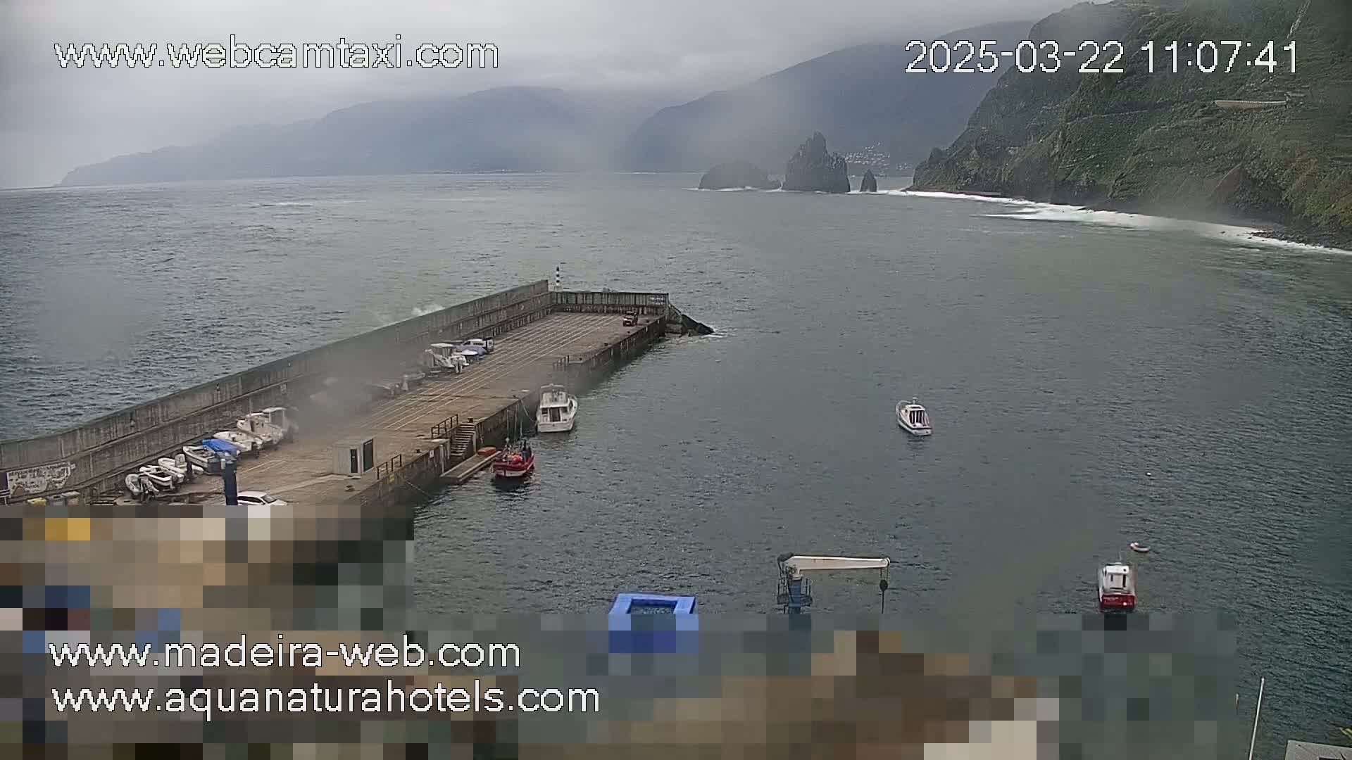 A small harbor with several boats is nestled against a rocky coastline under an overcast sky.
