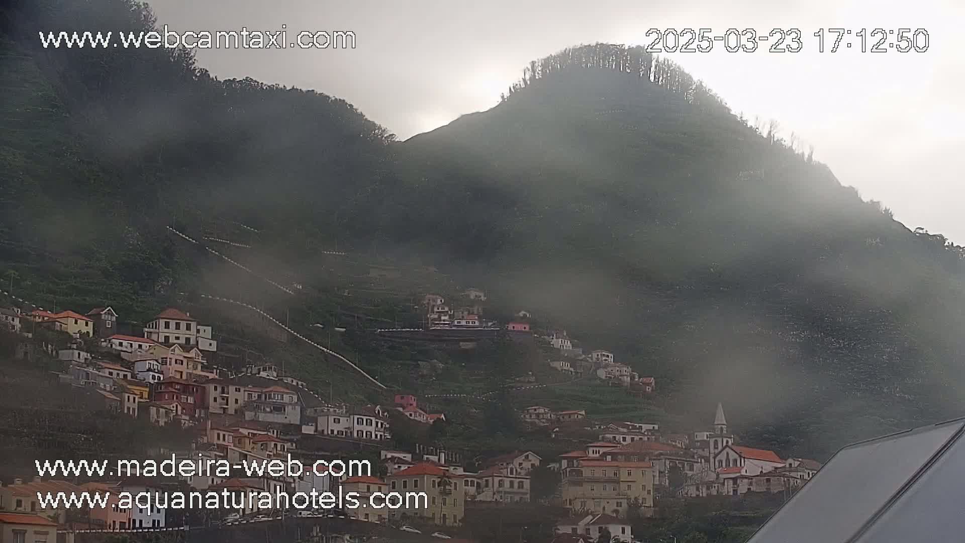 A misty hillside village clings to the slopes of a fog-shrouded mountain.