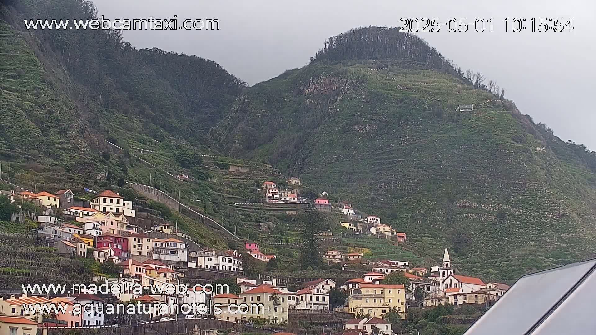 A hillside village of colorful houses clings to a steep, terraced mountainside under an overcast sky.