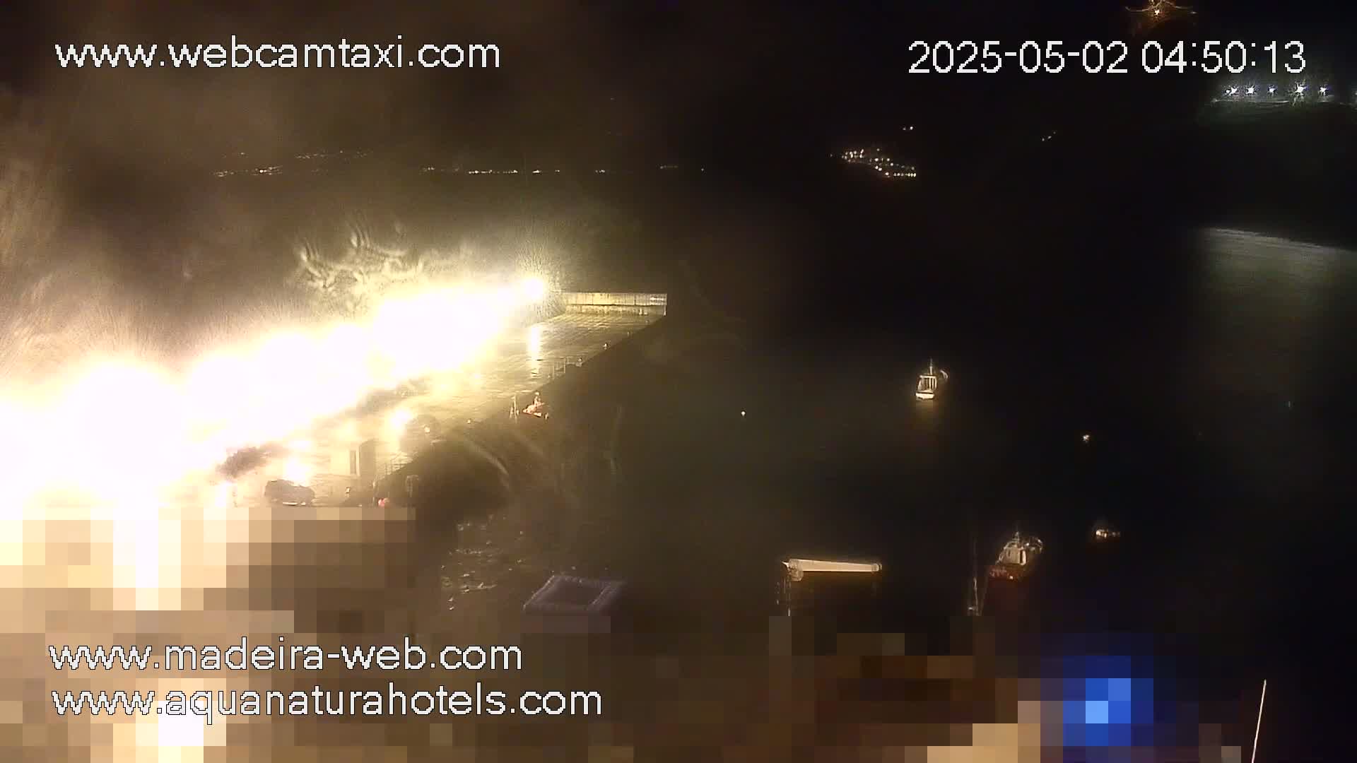 A nighttime harbor scene shows a brightly lit dock area amidst heavy spray and mist.