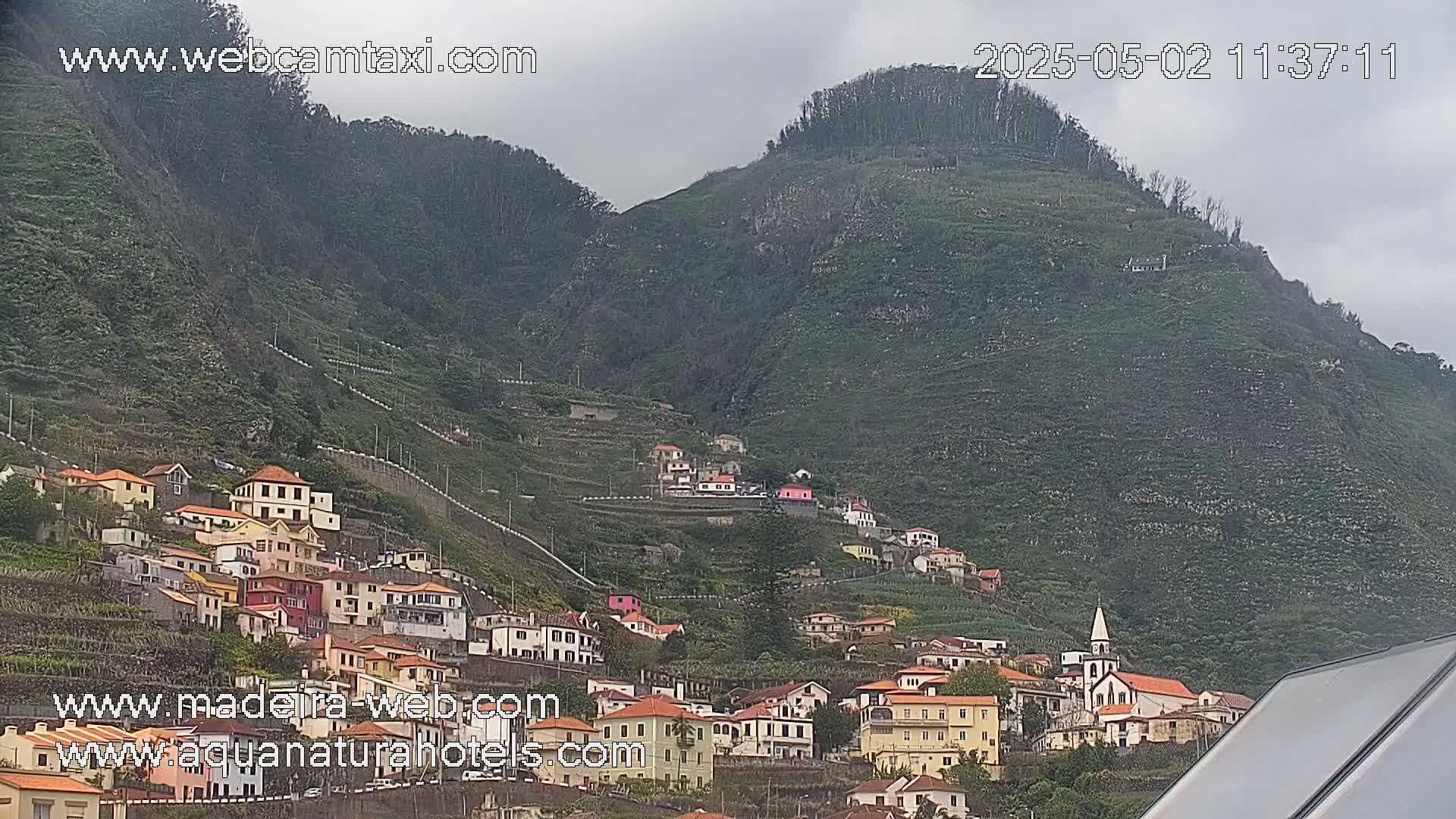 A village of colorful houses clings to the steep, green slopes of a mountain under an overcast sky.