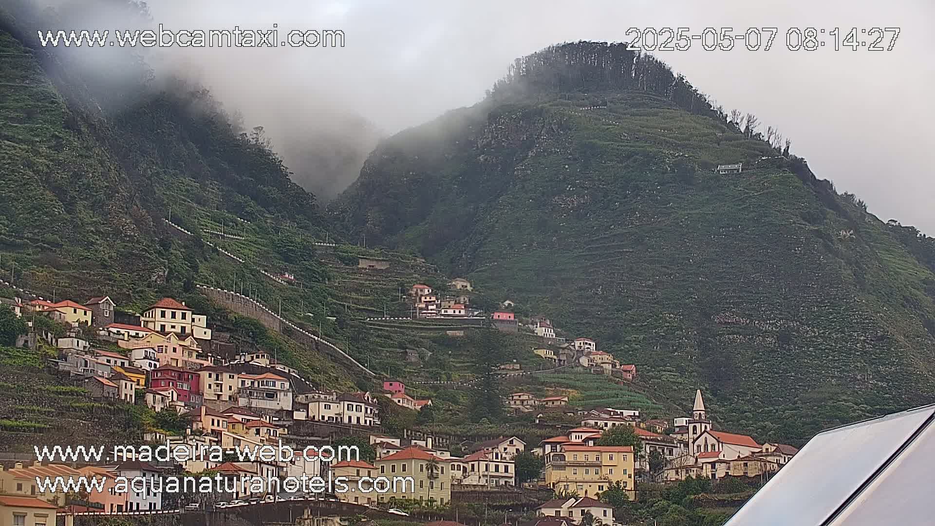 A village of colorful houses clings to a steep, terraced hillside shrouded in mist.
